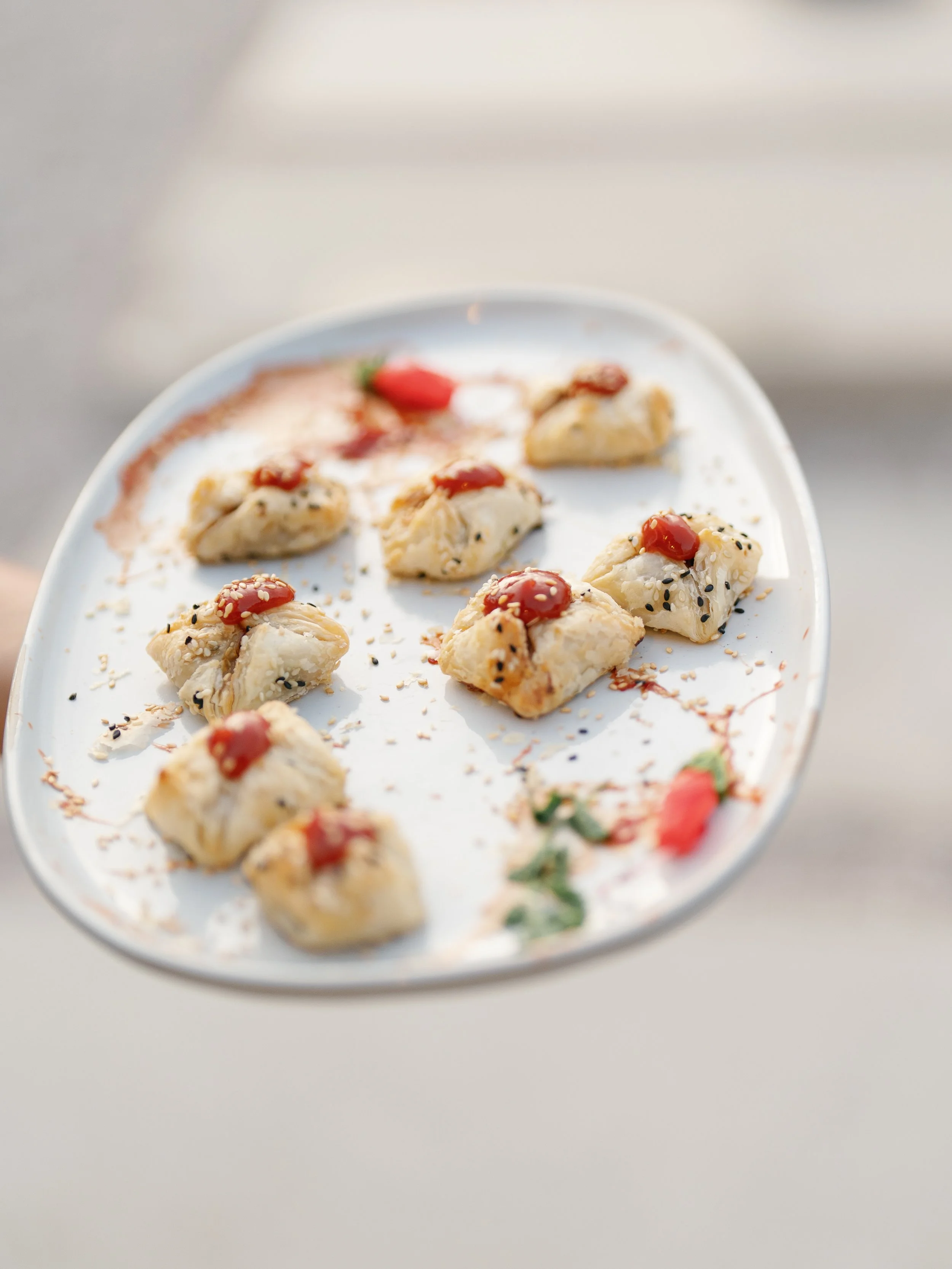 Plate of assorted dumplings topped with ketchup, black sesame seeds, and garnished with a small piece of decorated food shaped like a strawberry.