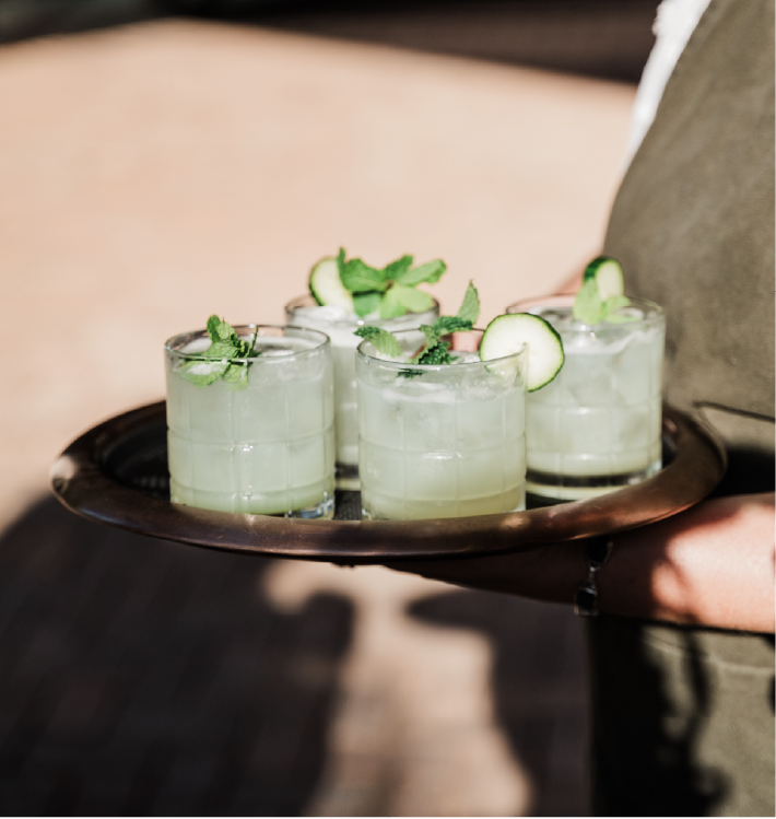 Four glasses of cucumber frose garnished with mint and cucumber slices on a round tray