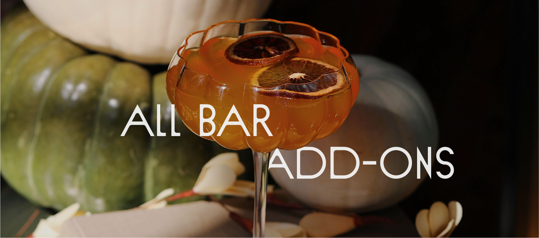 A cocktail glass filled with an orange drink garnished with dried citrus slices, with pumpkins in the background.