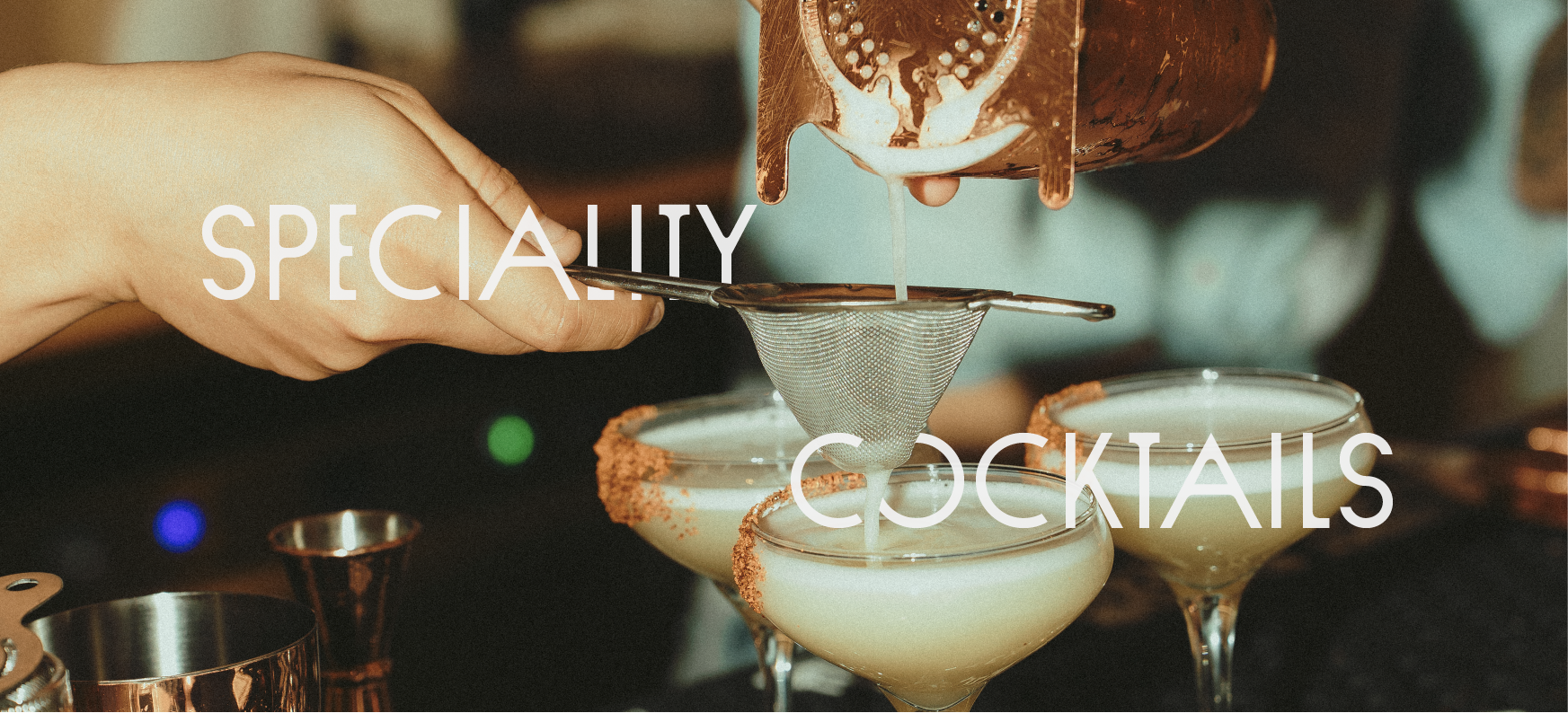 A bartender pouring cocktail mixture through a strainer into glasses with salted rim garnished drinks, with the overlay text 'SPECIALTY COCKTAILS'.