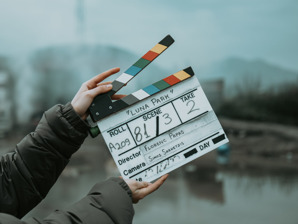Clapperboard for film production held outdoors with water and trees in the background.