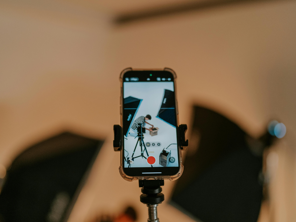 Smartphone mounted on a tripod recording a person arranging equipment in a studio.