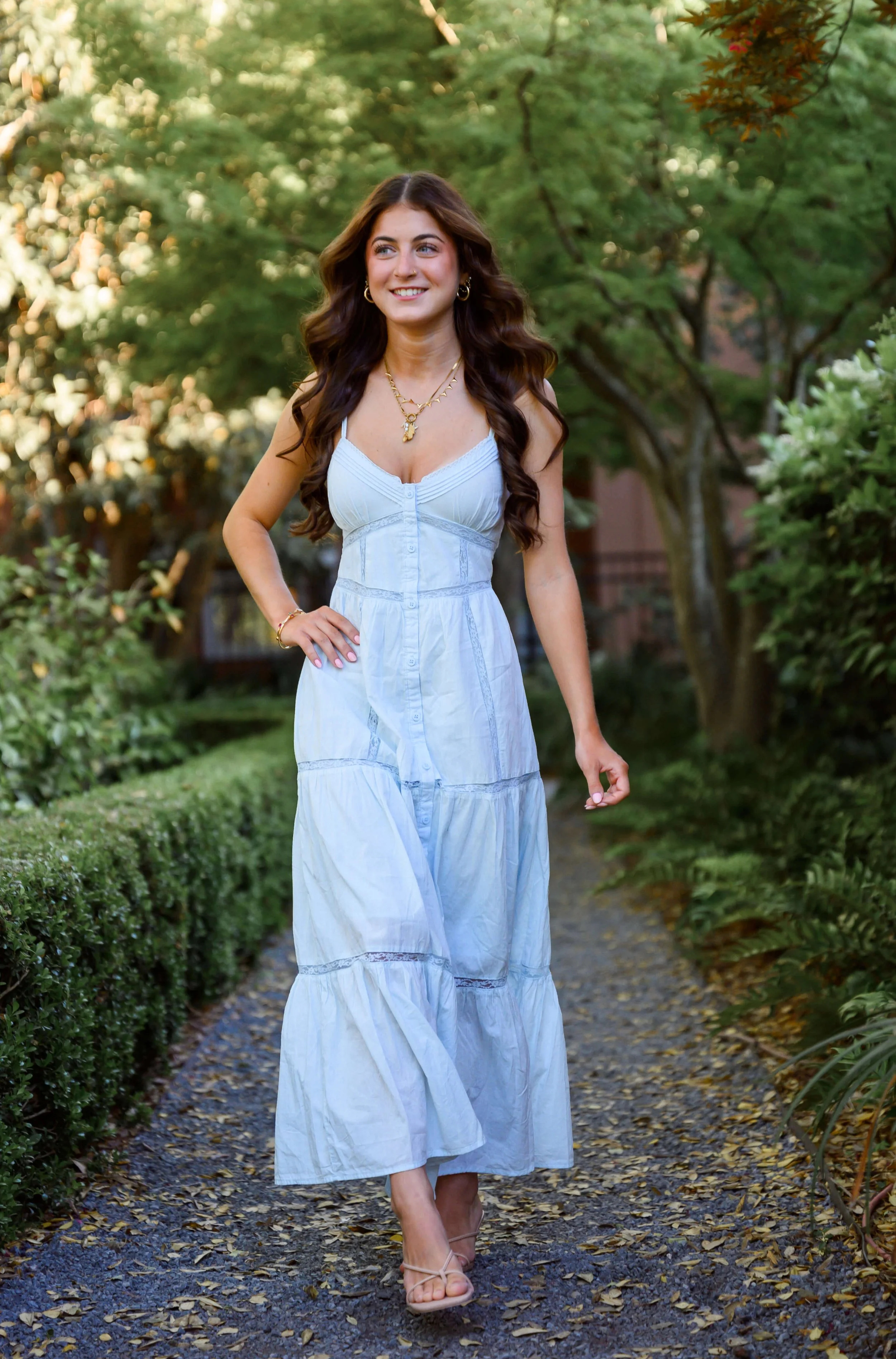 Charleston senior portrait on a quiet garden path surrounded by green hedges and trees.