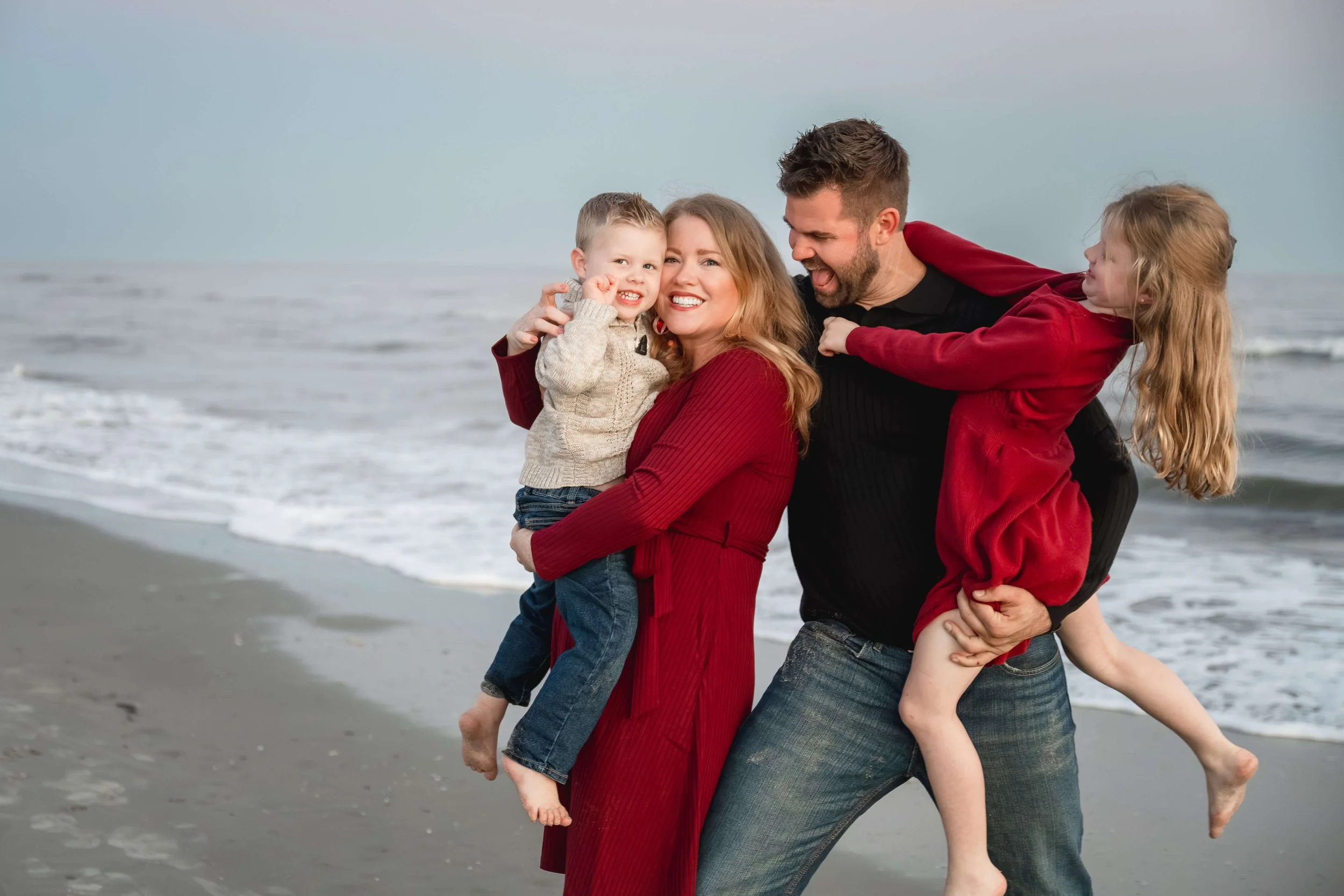 A father lifting his daughter in the air while the family laughs together on the beach.