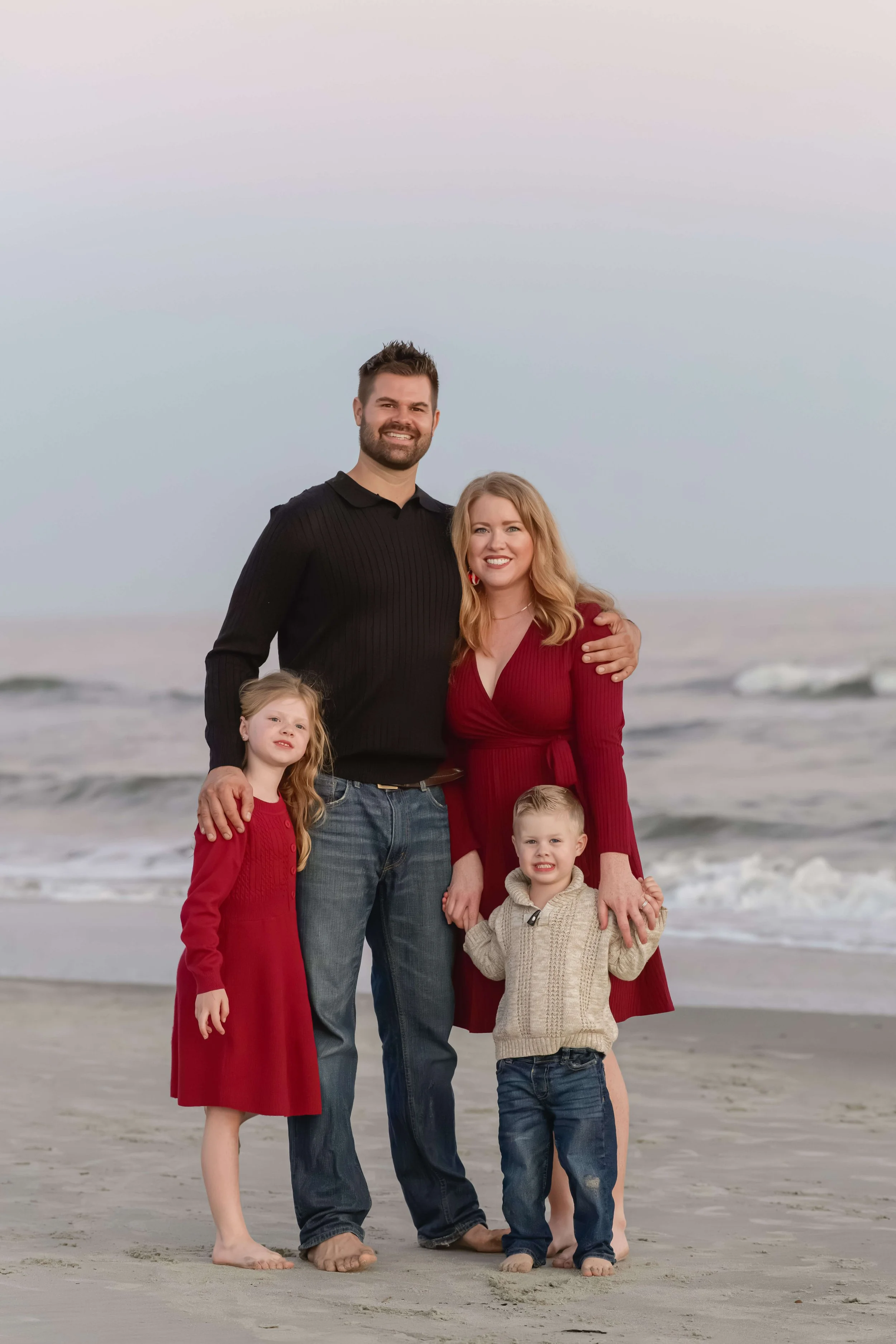Family of four standing near the ocean waves during a fall beach photography session in South Carolina.