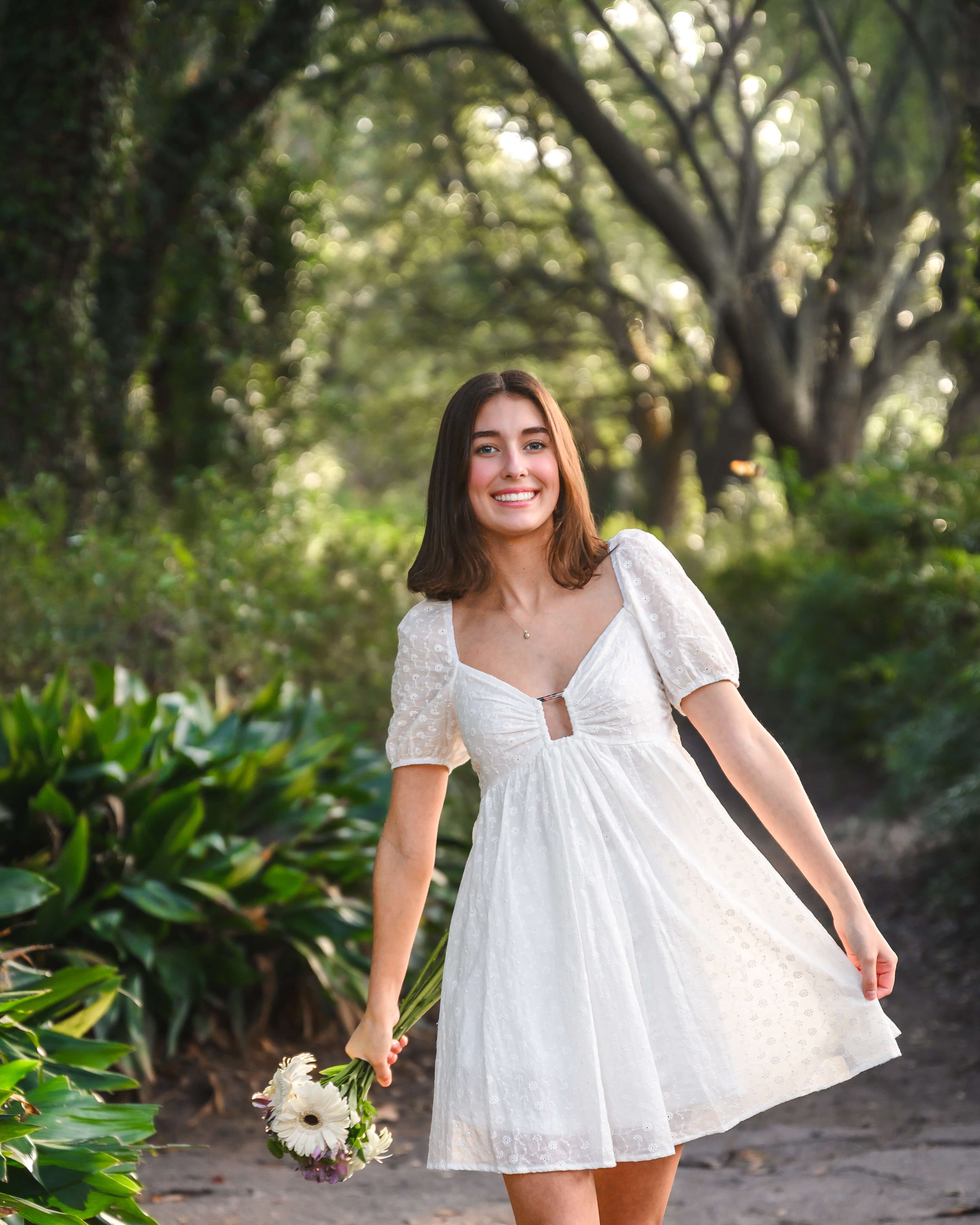 Smiling girl holding bouquet of flowers on path at Hampton Park for senior photos