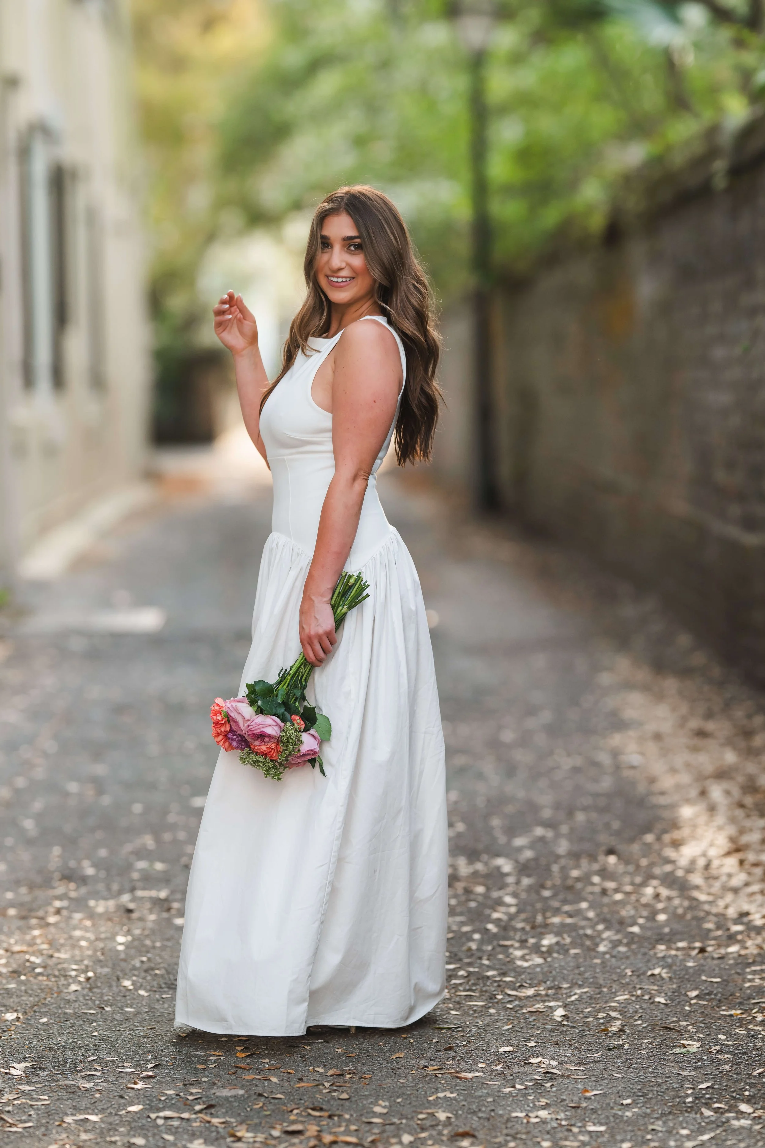 Charleston School of Law Grad Student in light-filled alley with white dress and bouquet of flowers