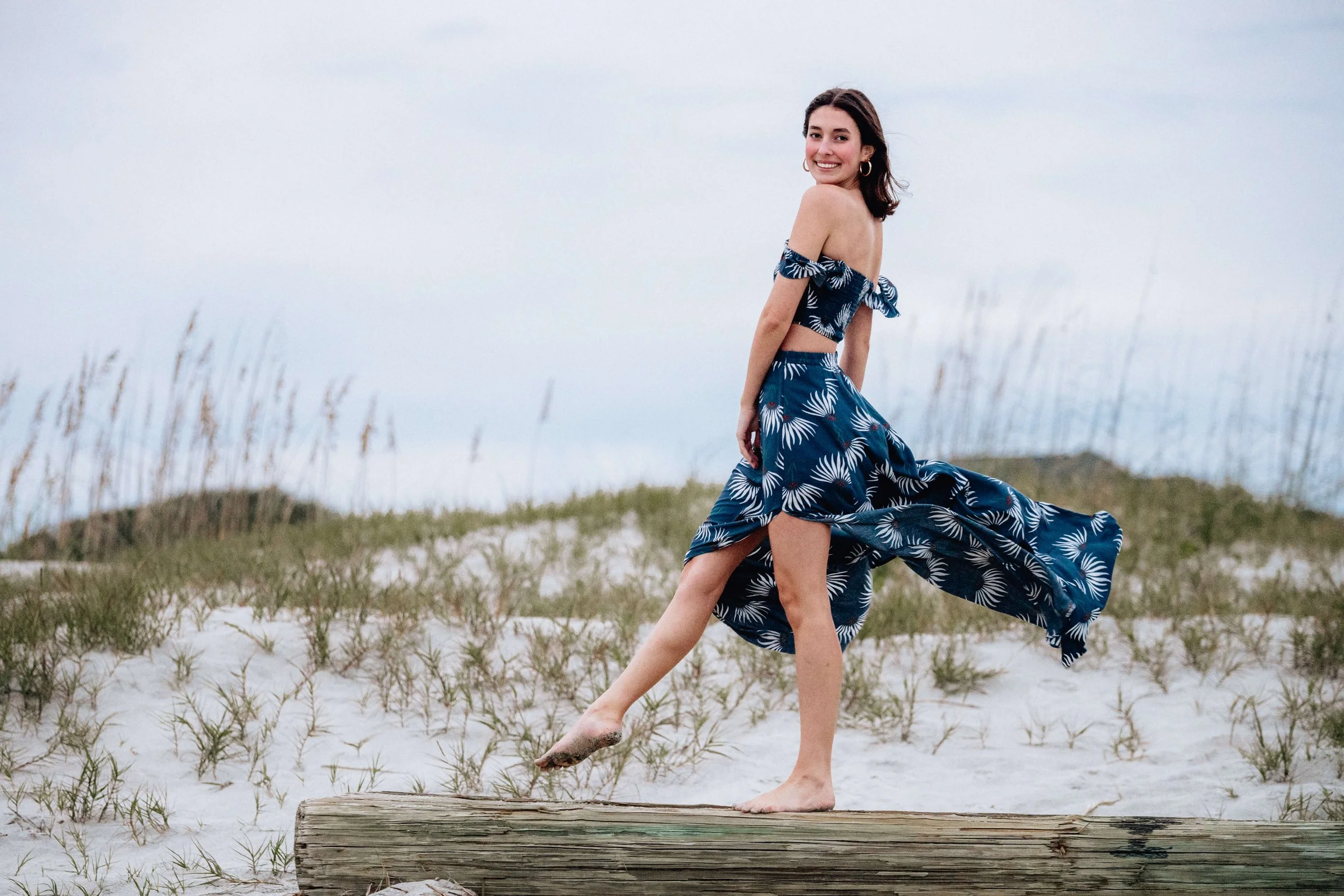 girl walking on log at beach at sunset smiling.