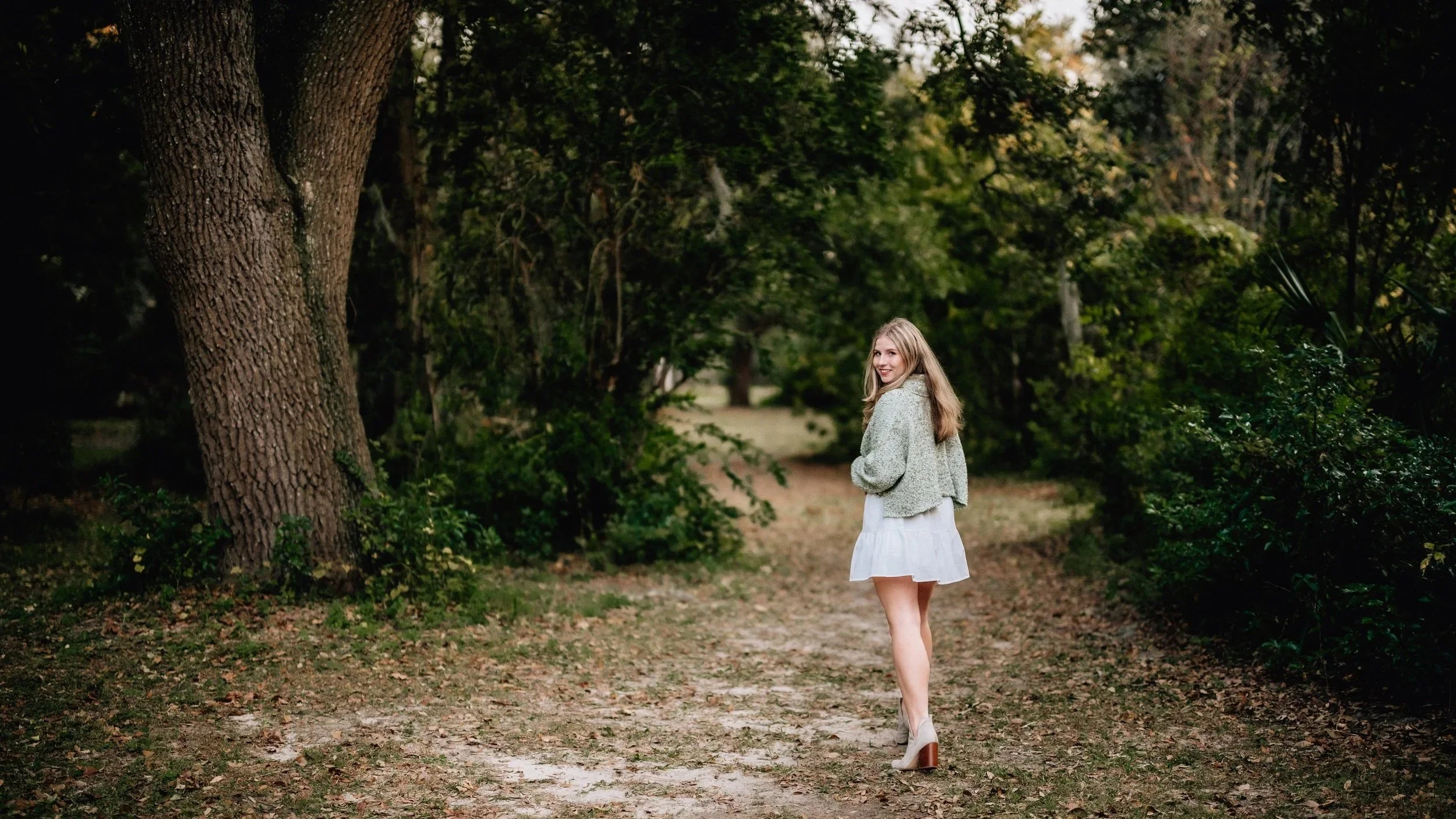 Girl in green sweater and white dress during fall on a path in woods