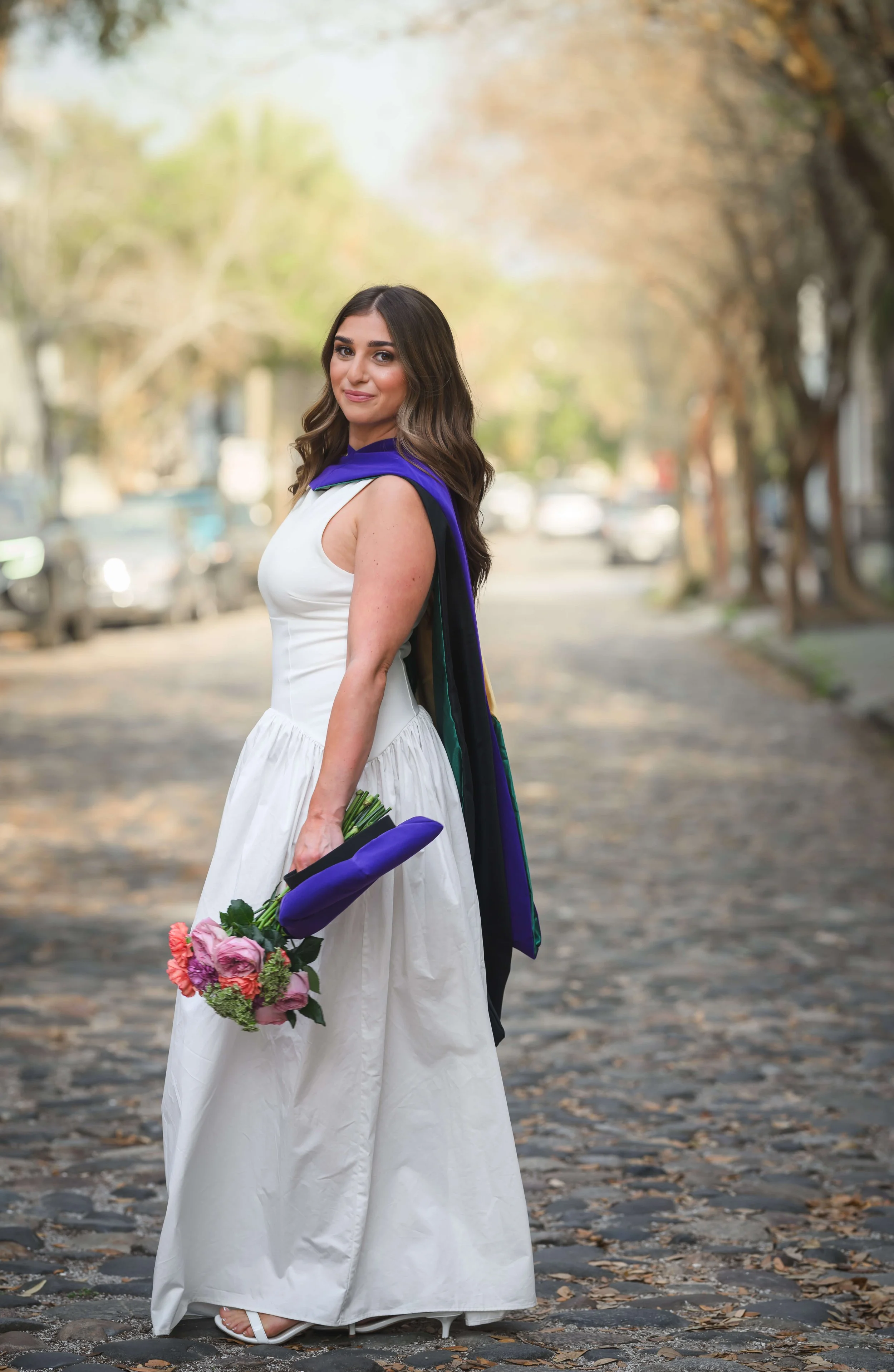 Charleston School of Law Grad Student on Chalmers Street in hood holding a bouquet of flowers.