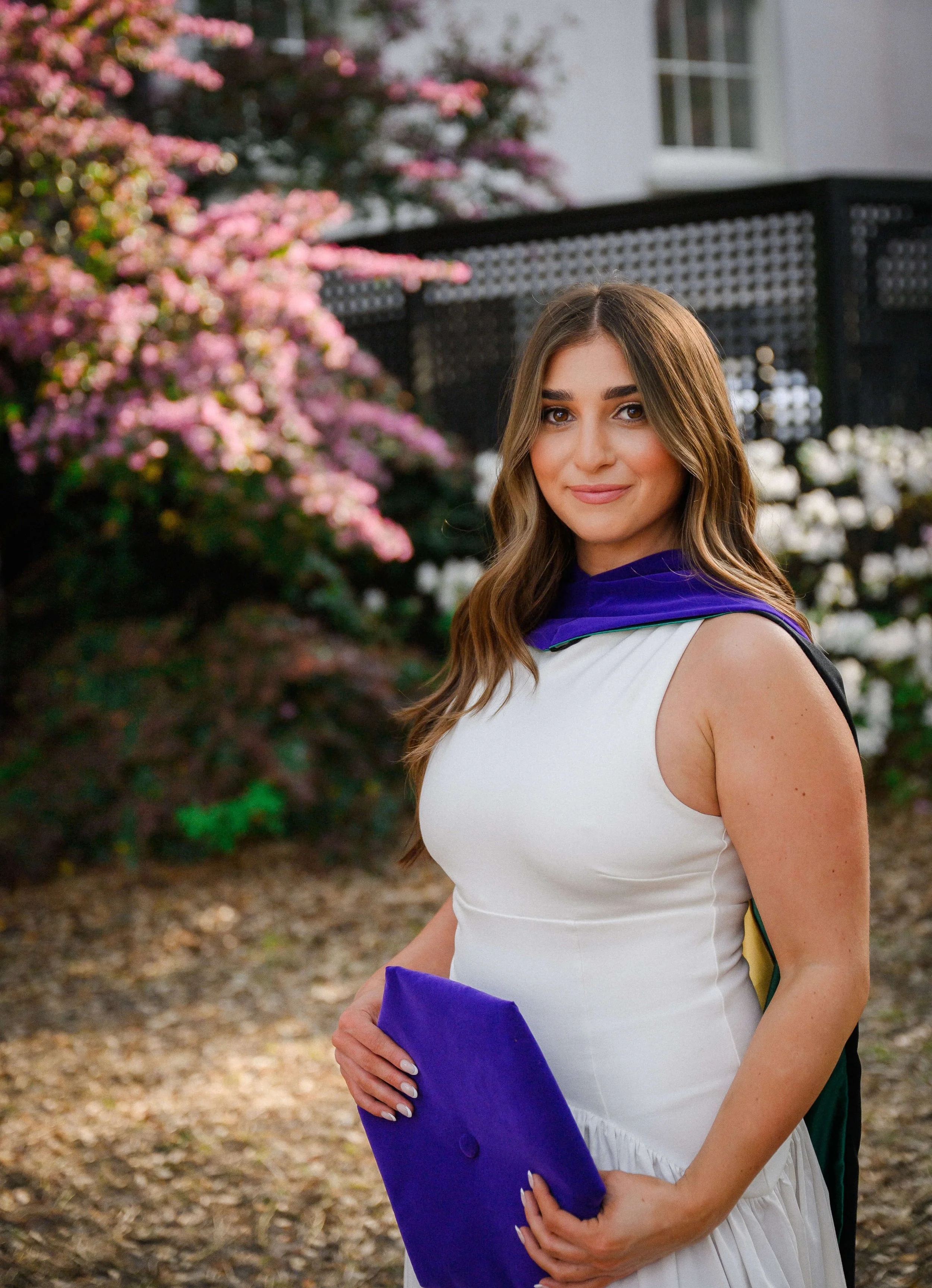 Charleston School of Law Grad Student holding cap and wearing hood with flowers behind her