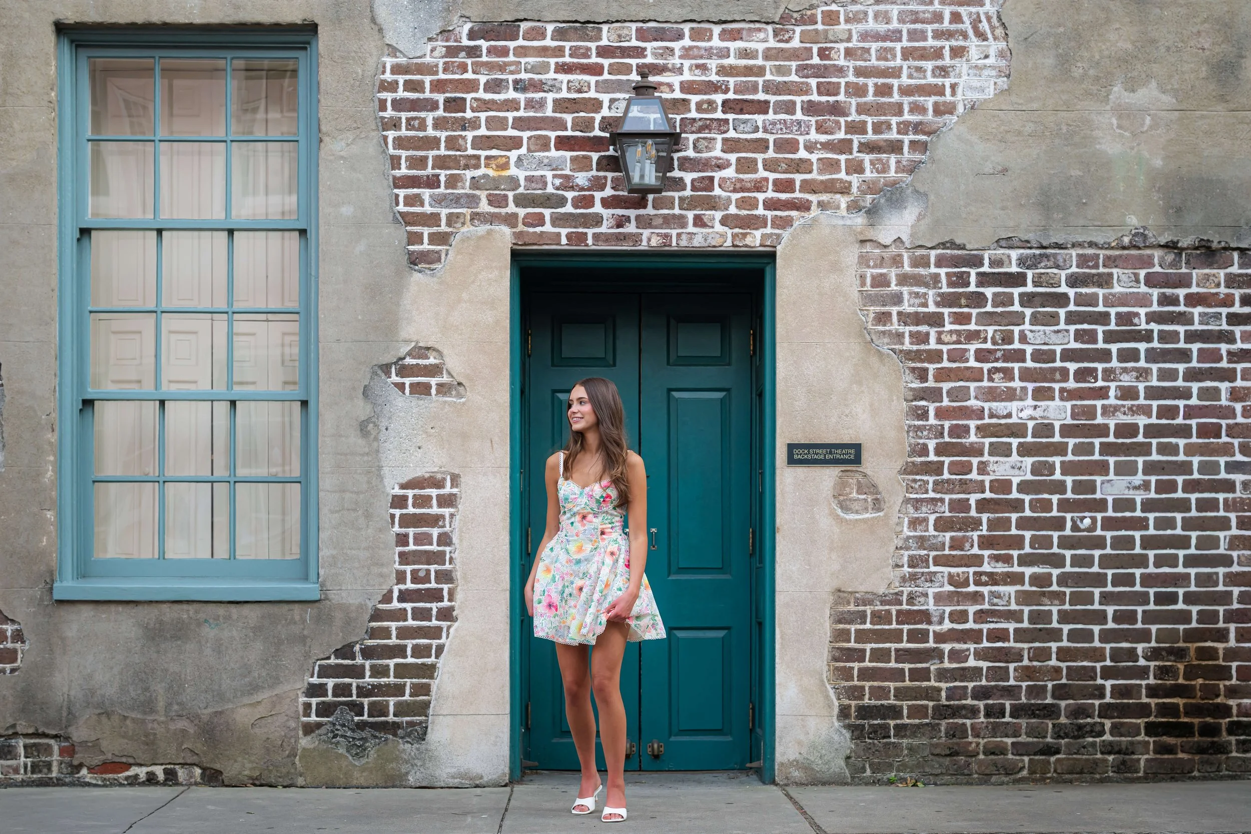 high school senior in dress posing in front of a brick wall at the Dock St. Theater in Charleston.
