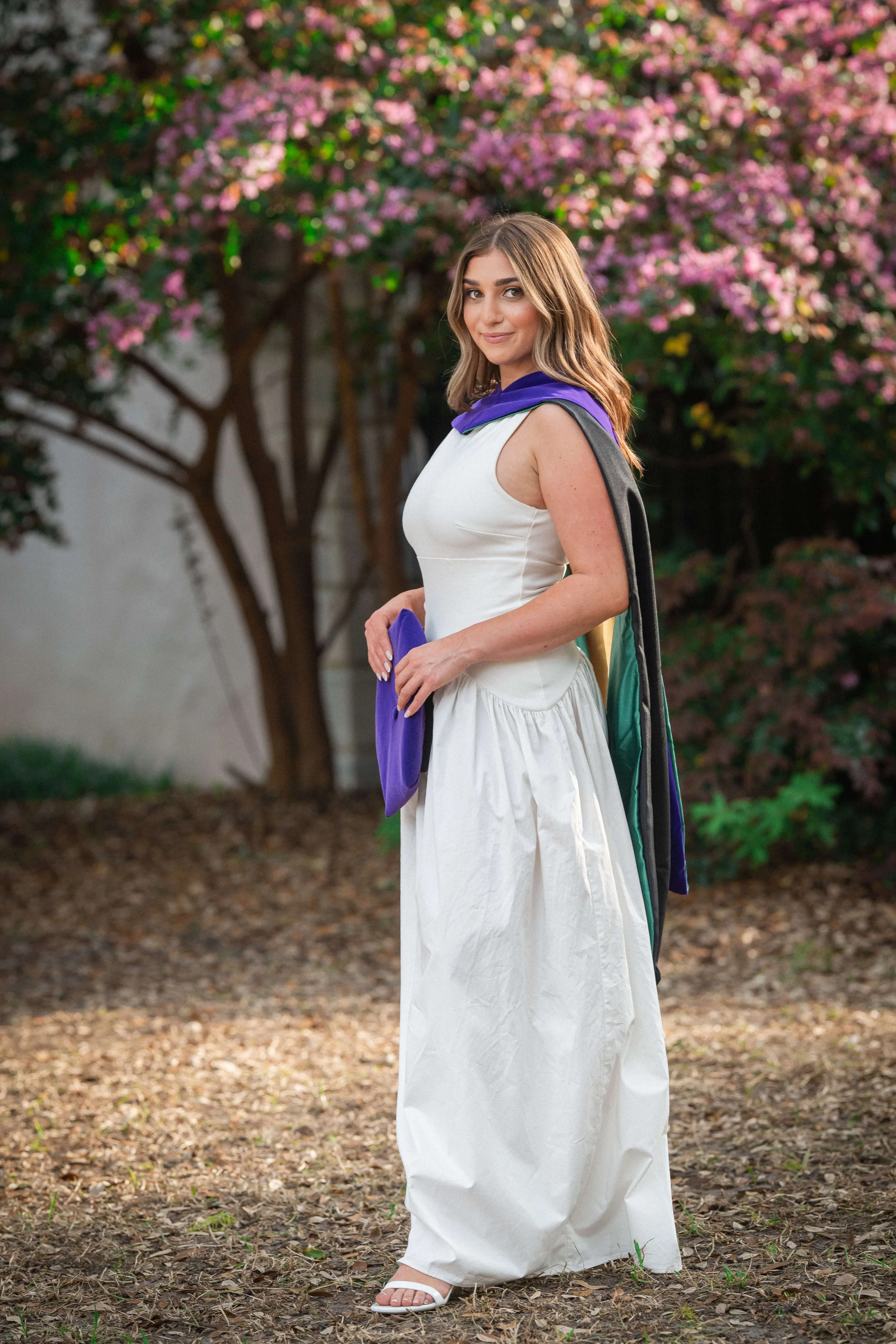 Charleston School of Law Grad Student standing with cap and smiling at camera with pink flowering tree behind her