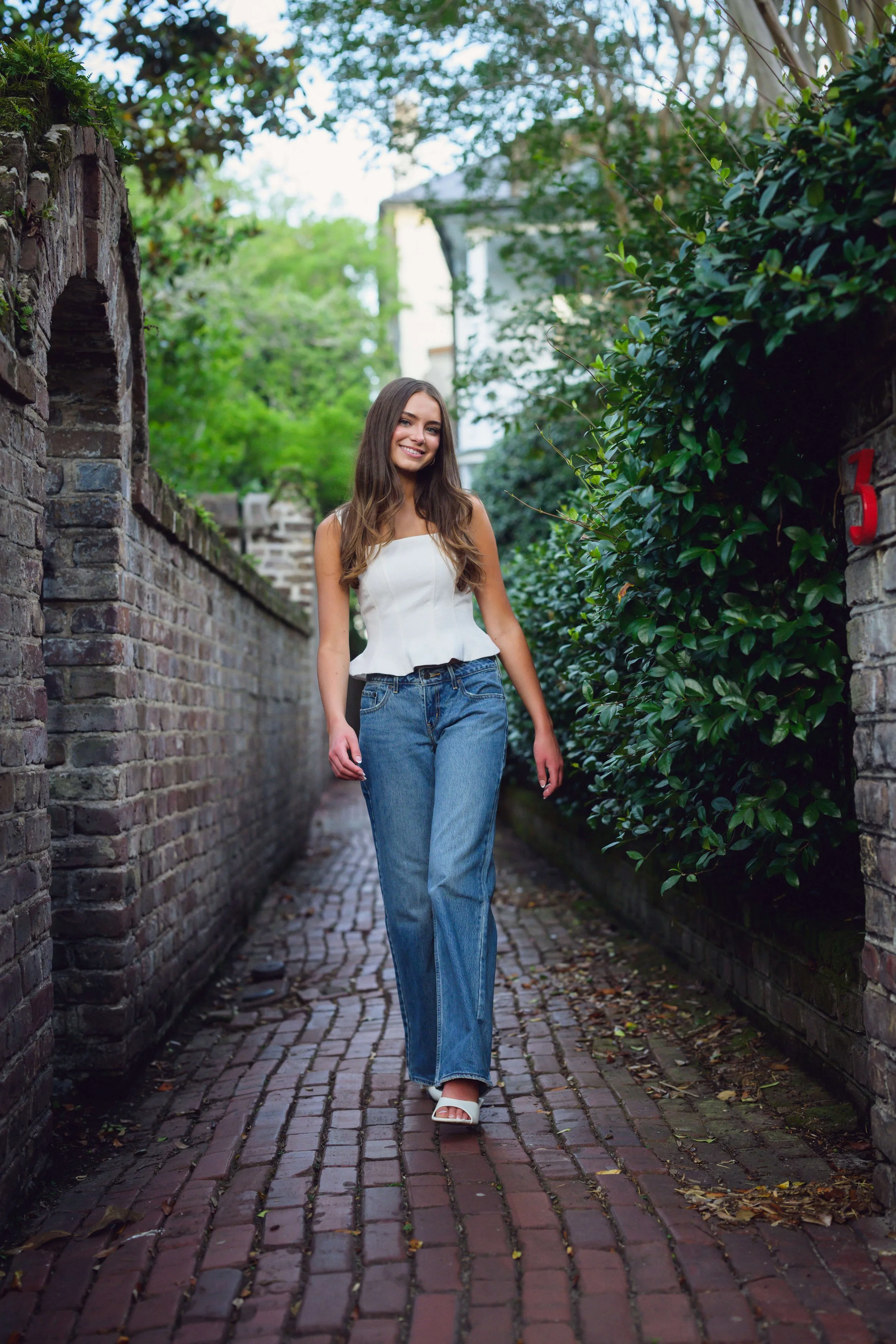 High School Senior posing in Stolls Alley in Charleston, SC in blue jeans and white top