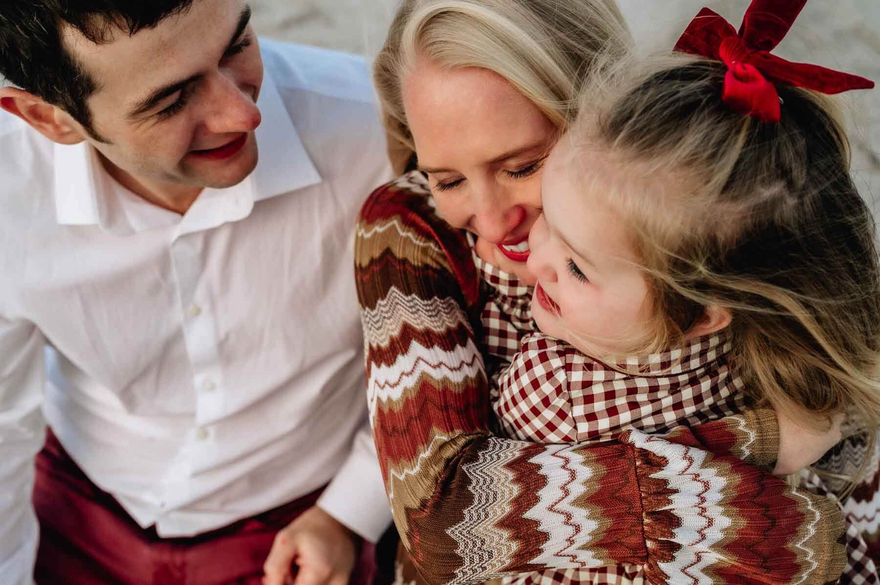 A family of three hugging and smiling outdoors.
