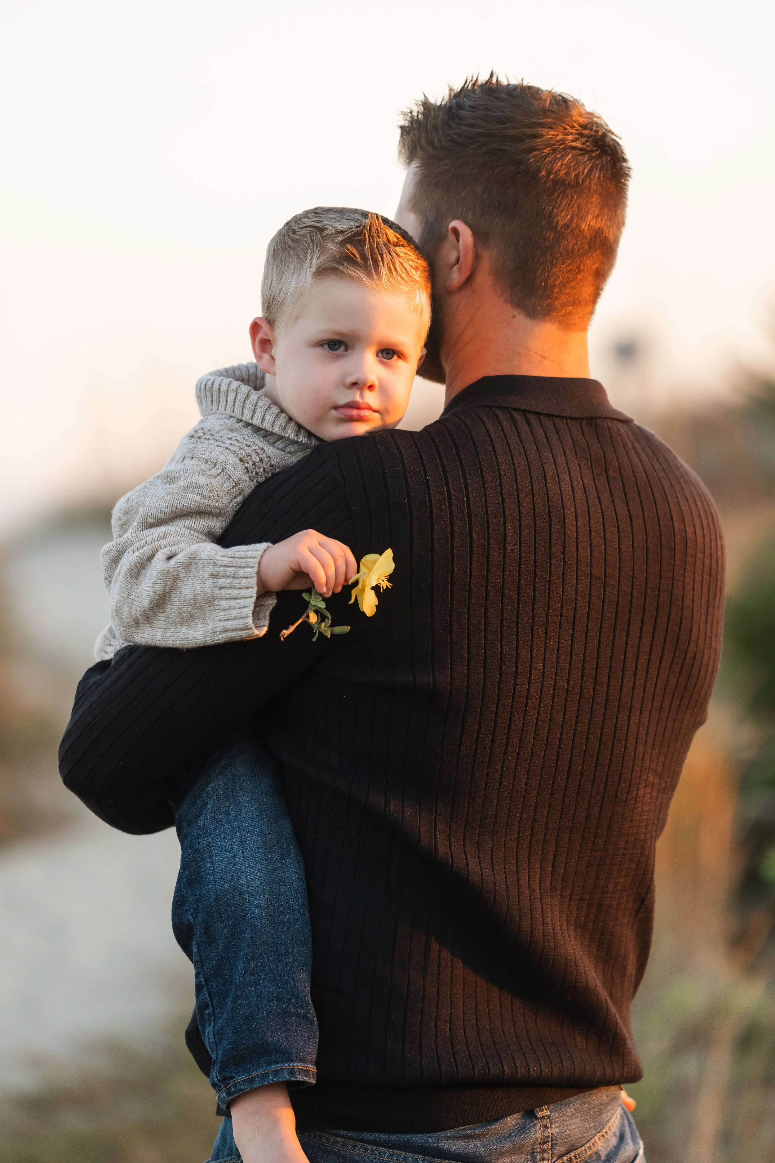 A young boy looking over his father's shoulder during a sunset family photography session.