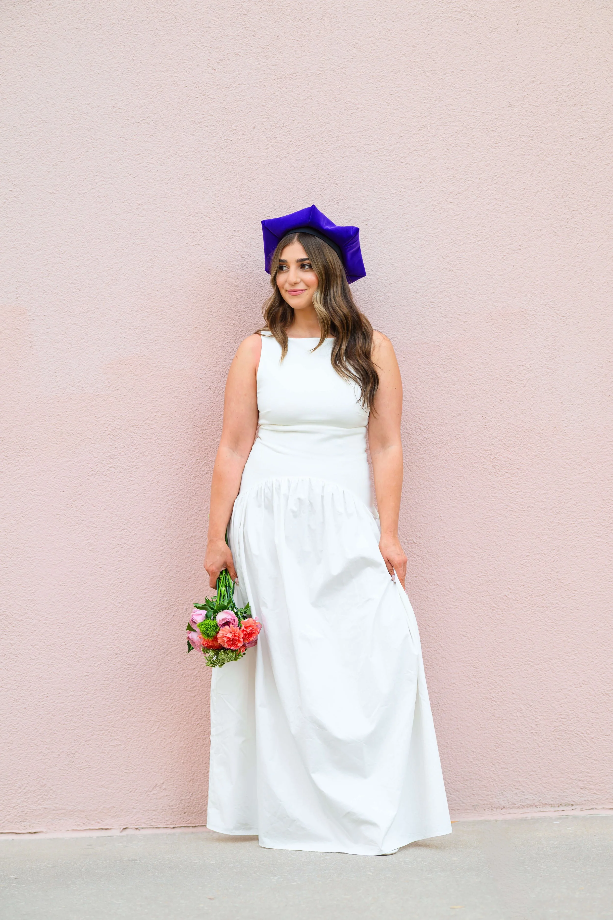 Charleston School of Law Grad Student holding bouquet of flower and wearing white dress and purple graduation cap