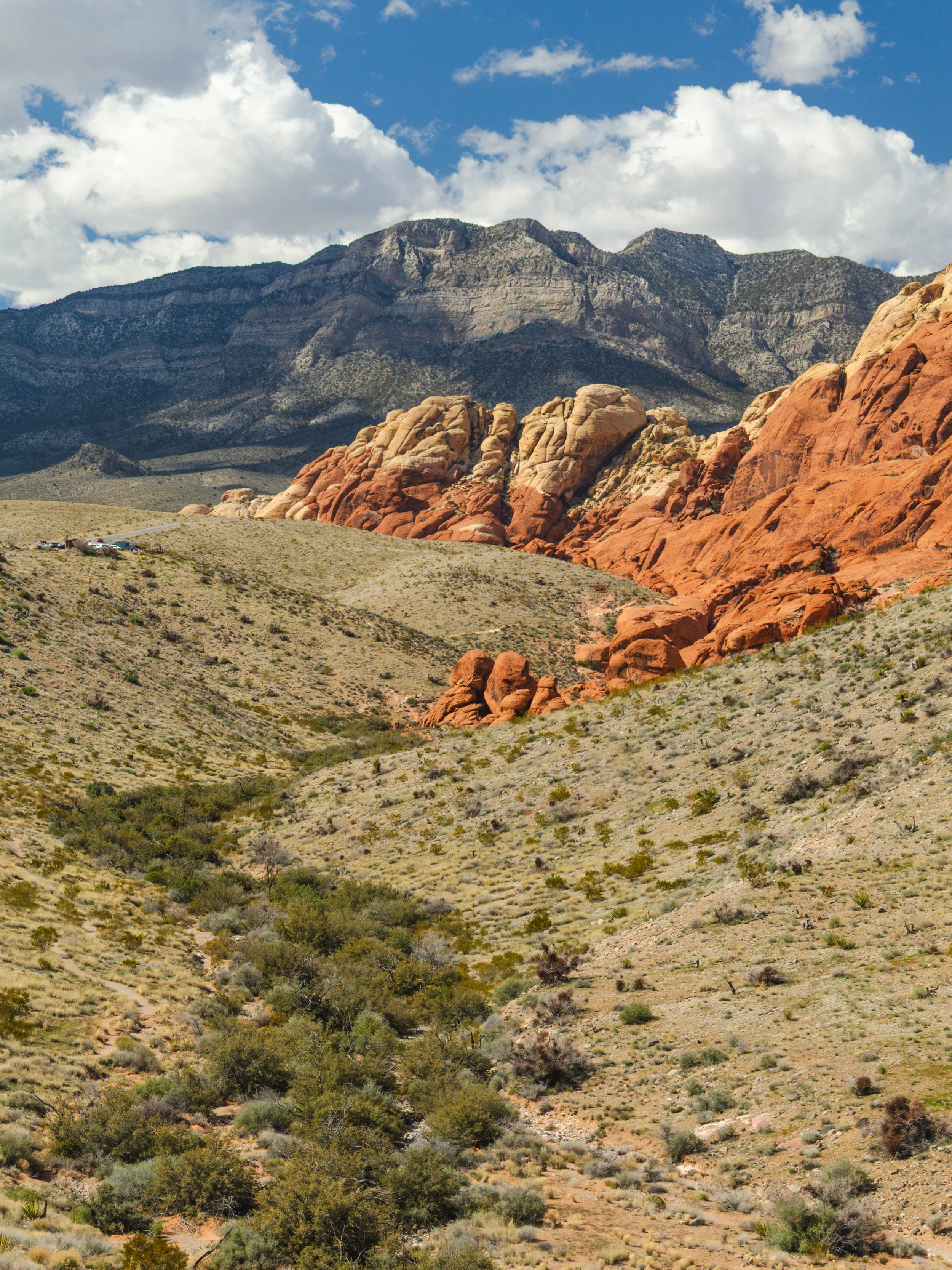 A landscape of a desert with rocky formations and mountains in the background, under a partly cloudy sky.