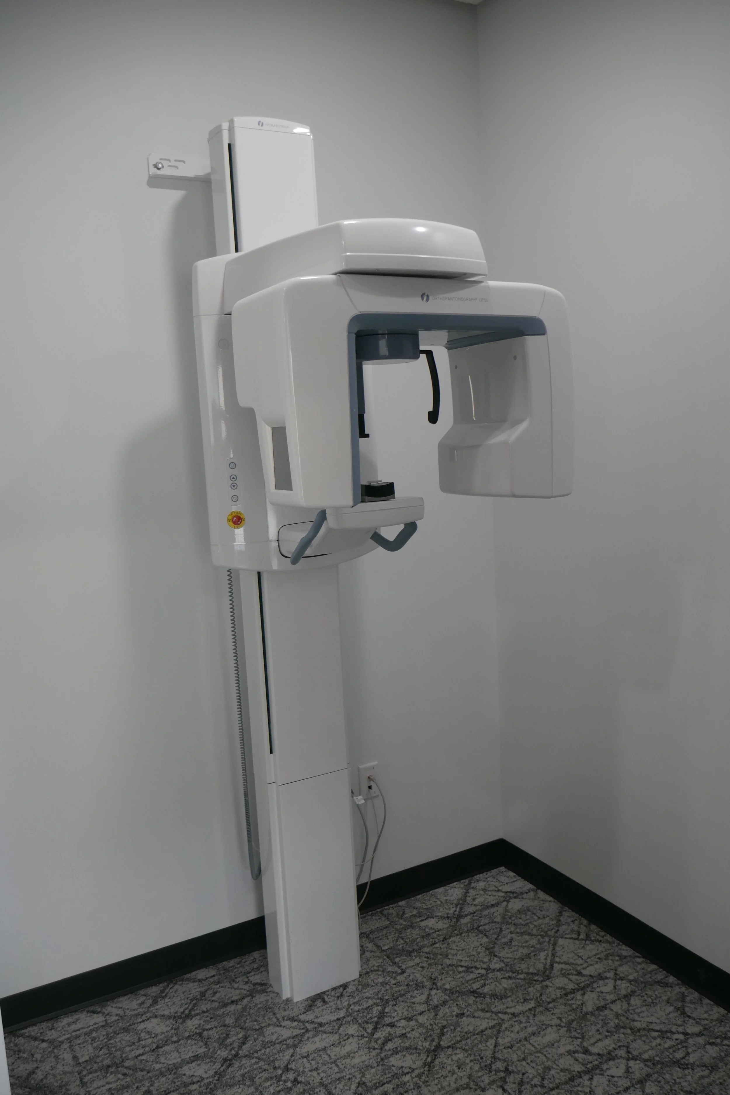 Medical X-ray machine in a room with gray walls and patterned carpet.