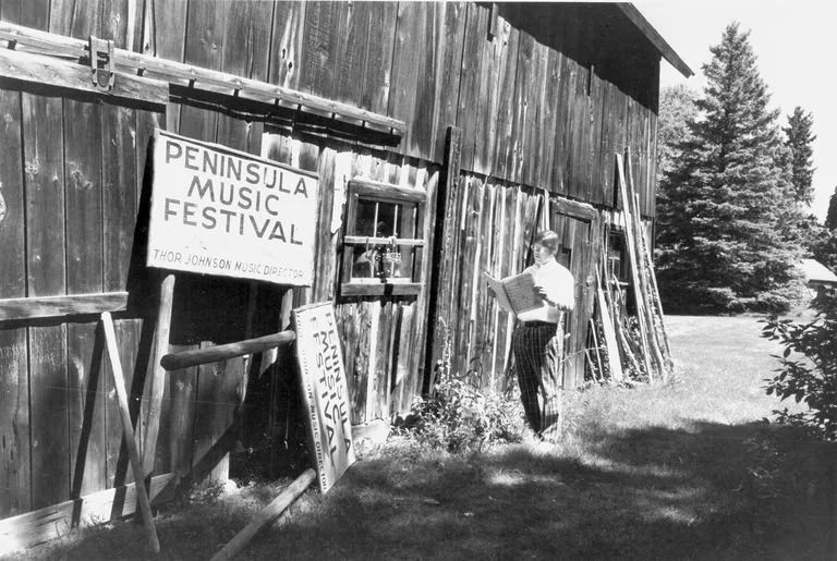Photo: B&W  Standing man holding sheet music outside Anderson Barn; 2 signs leaning against barn read "Peninsula Music Festival, Thor Johnson, Music Director;
Collection
Thor Johnson Collection (2013.007)