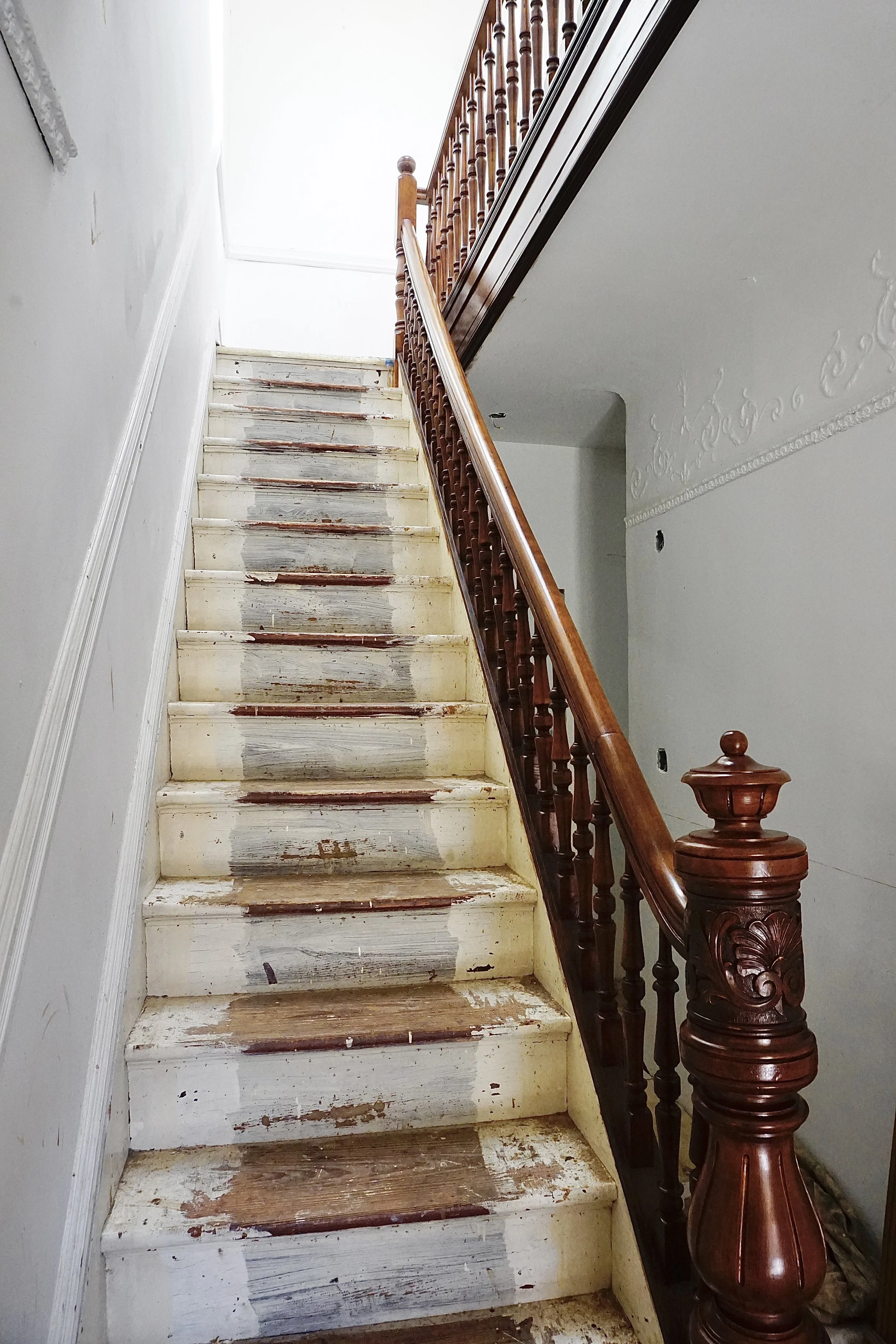 A staircase with worn, paint-chipped steps and a polished wooden handrail inside a house.