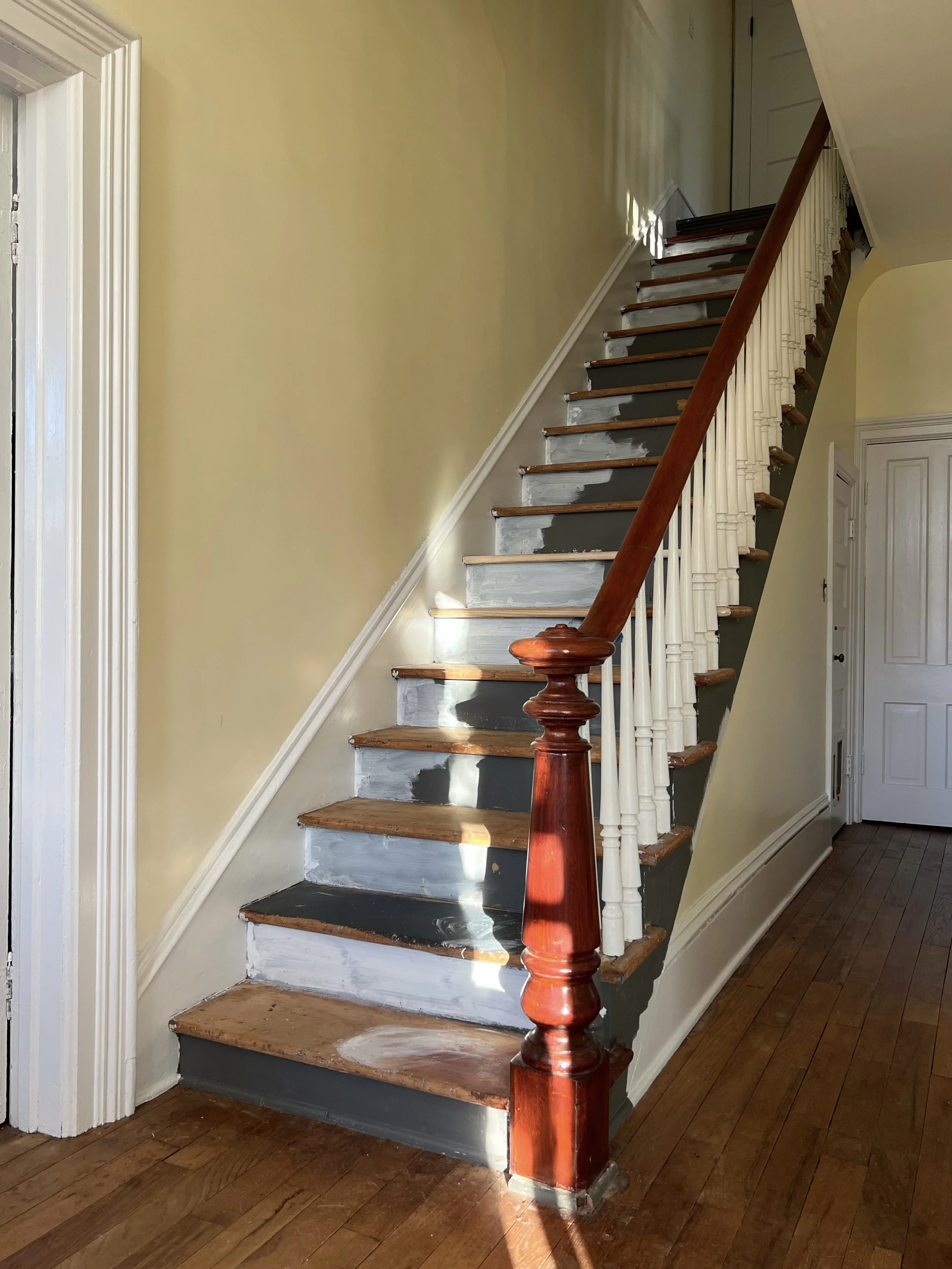 Unfinished wooden staircase with partially painted steps inside a house.