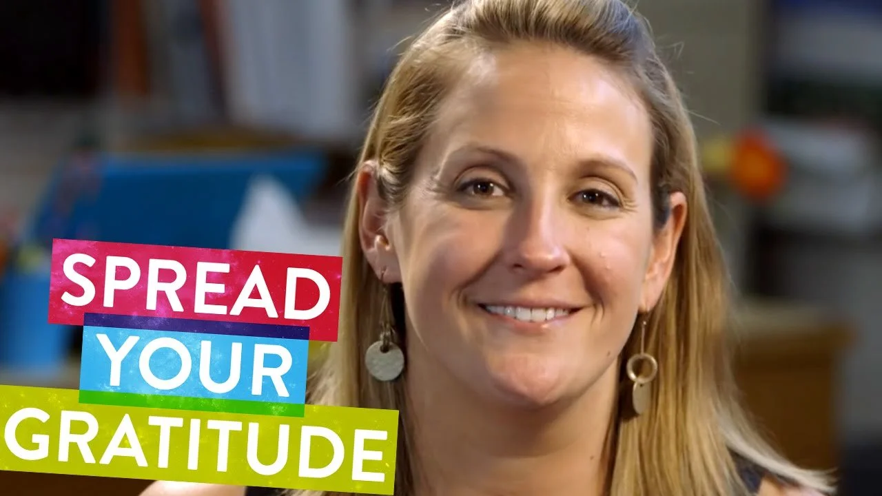 A smiling woman with blonde hair wearing earrings in a room with blurred background. Overlaid text says 'SPREAD YOUR GRATITUDE' in colorful blocks.