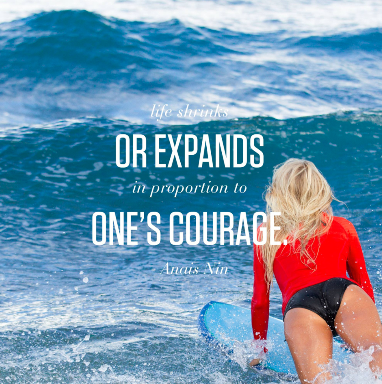 A woman in a red long-sleeve top and black shorts is surfing on a blue surfboard in the ocean, with waves in the background and an inspirational quote overlaid that reads: 'Life shrinks or expands in proportion to one's courage' by Anais Nin.