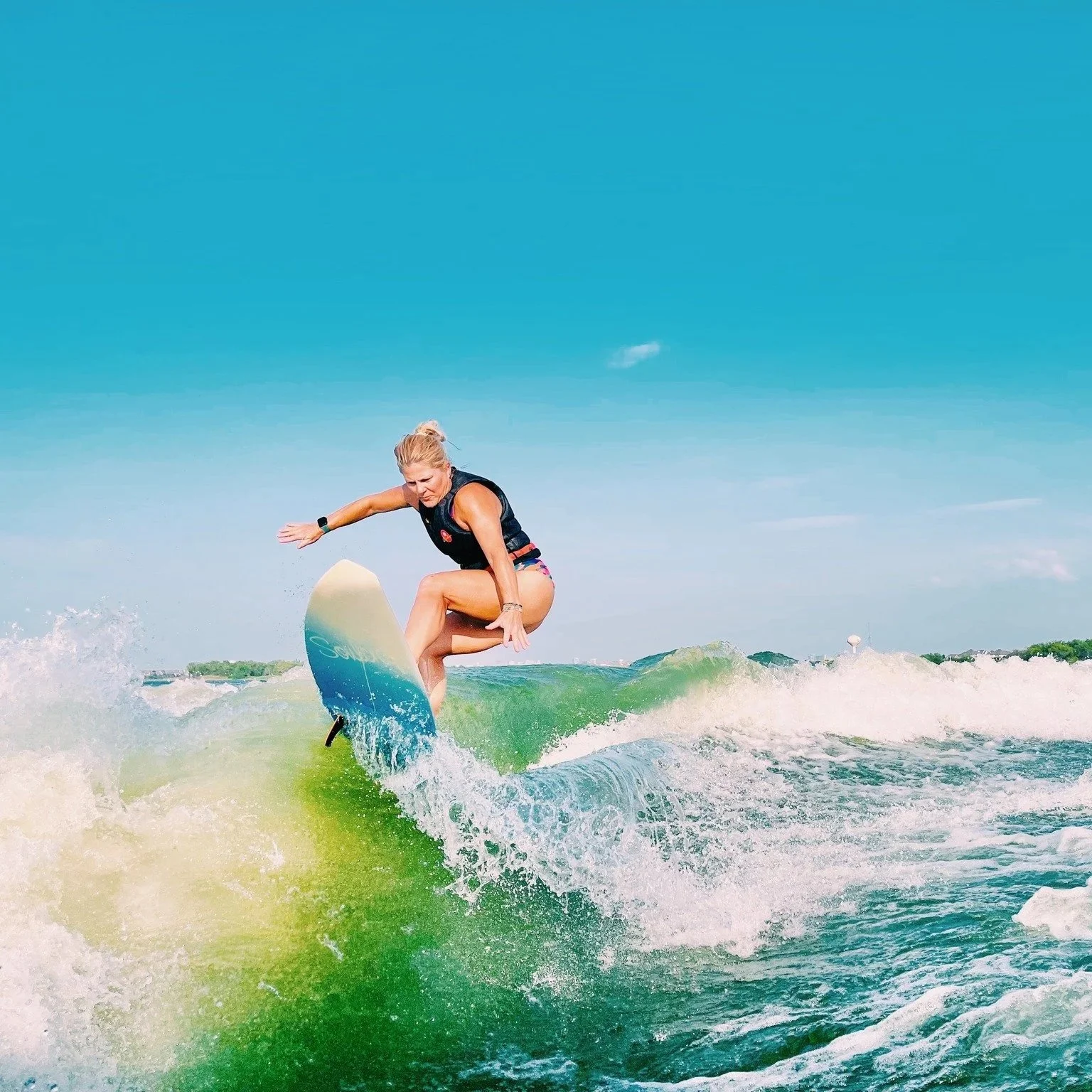 Woman surfing on a wave in the ocean under a clear blue sky.