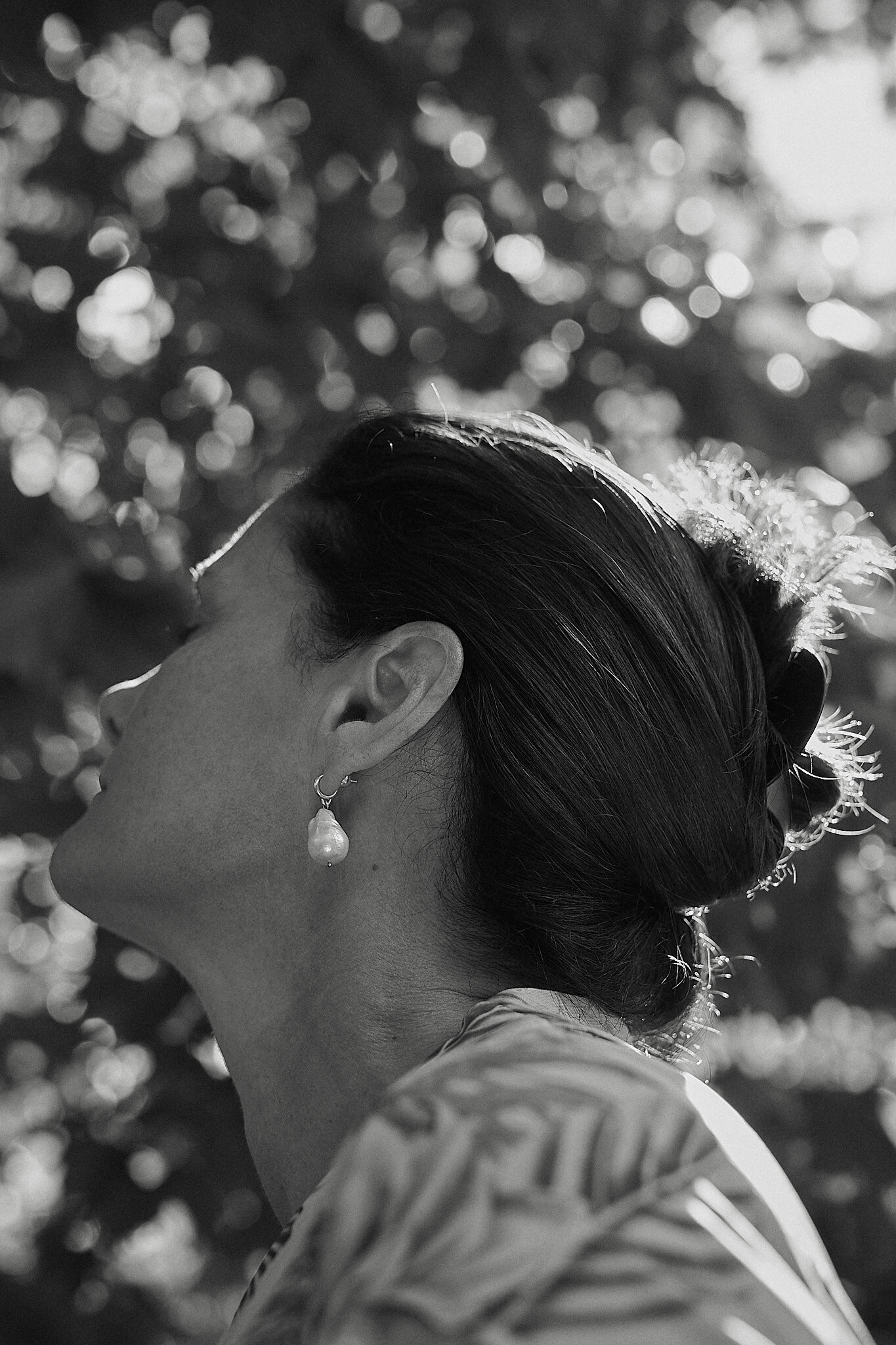 A black and white photograph of a woman with styled hair and an earring, captured in profile against a background of blurry bokeh light spots.