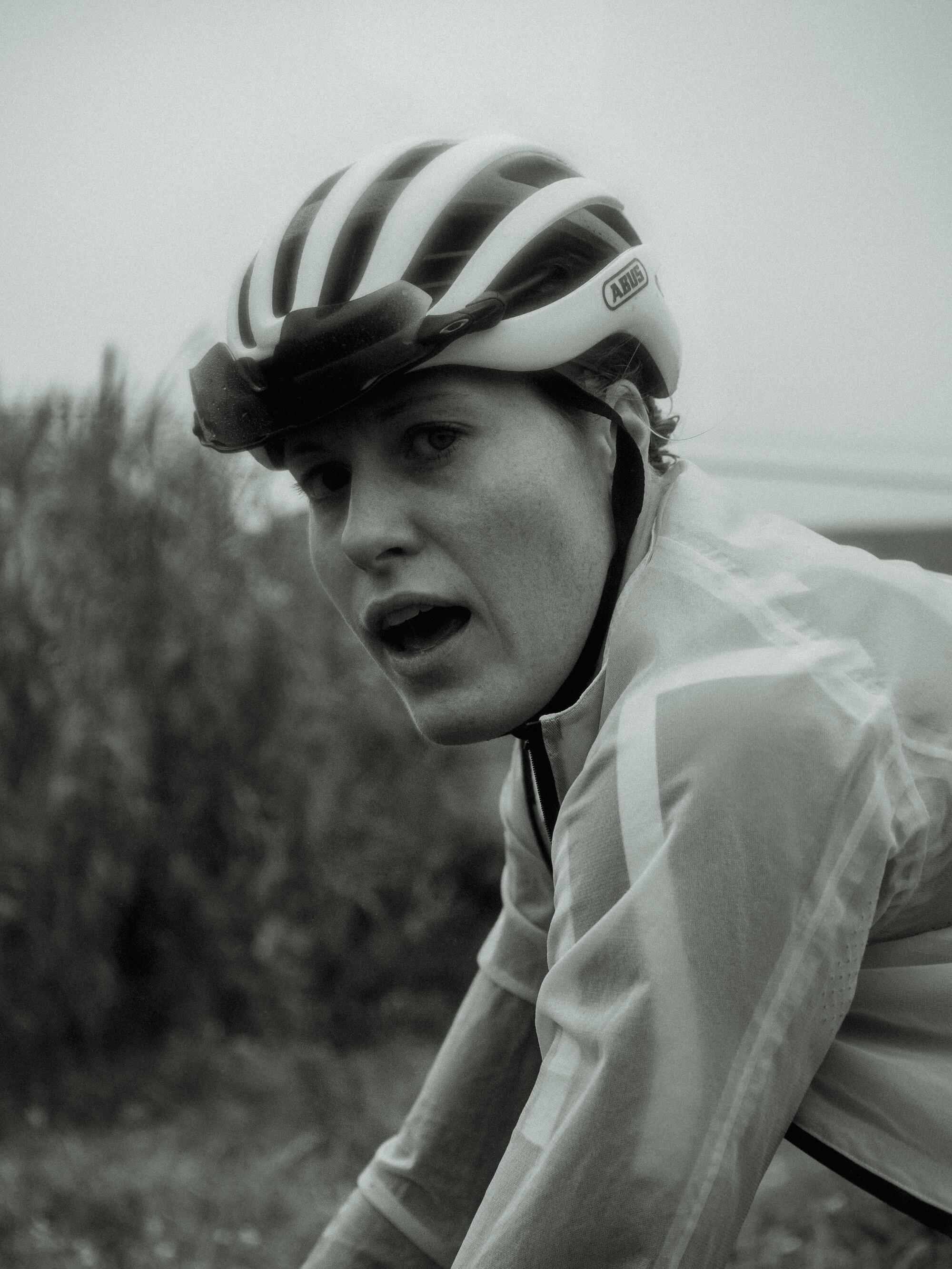 A young person in cycling gear wearing a helmet, with mouth open, outdoors in a natural setting.