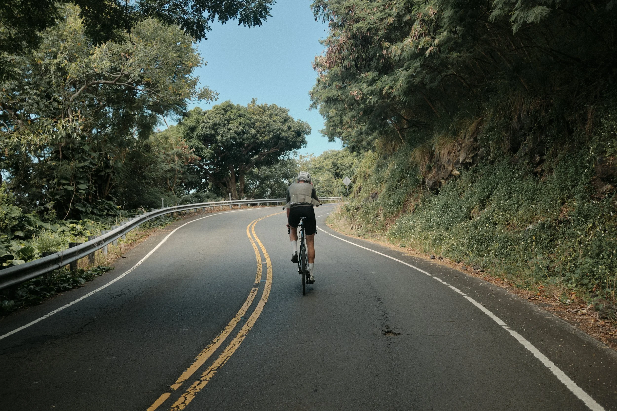 A person riding a bicycle on a winding road surrounded by trees and greenery during the daytime.