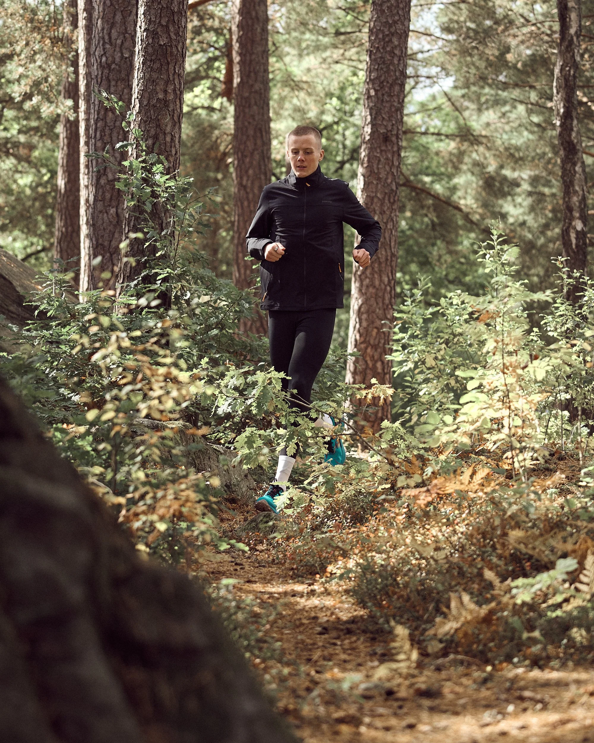 A person running through a forest trail surrounded by tall trees and green foliage.