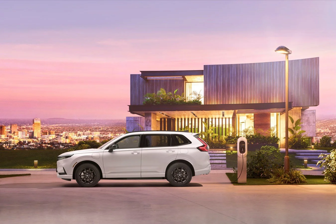 A white SUV parked in front of a modern house at sunset, with an electric vehicle charging station nearby and city skyline in the background.