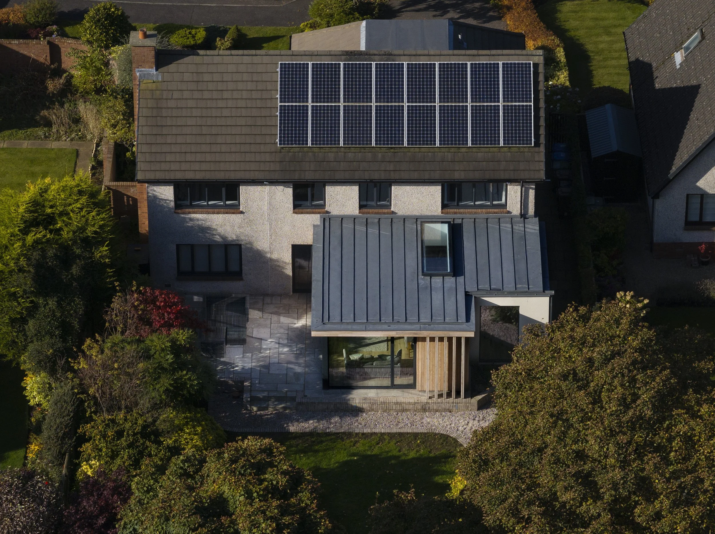 An aerial view of a house with solar panels on the roof, surrounded by greenery and trees.