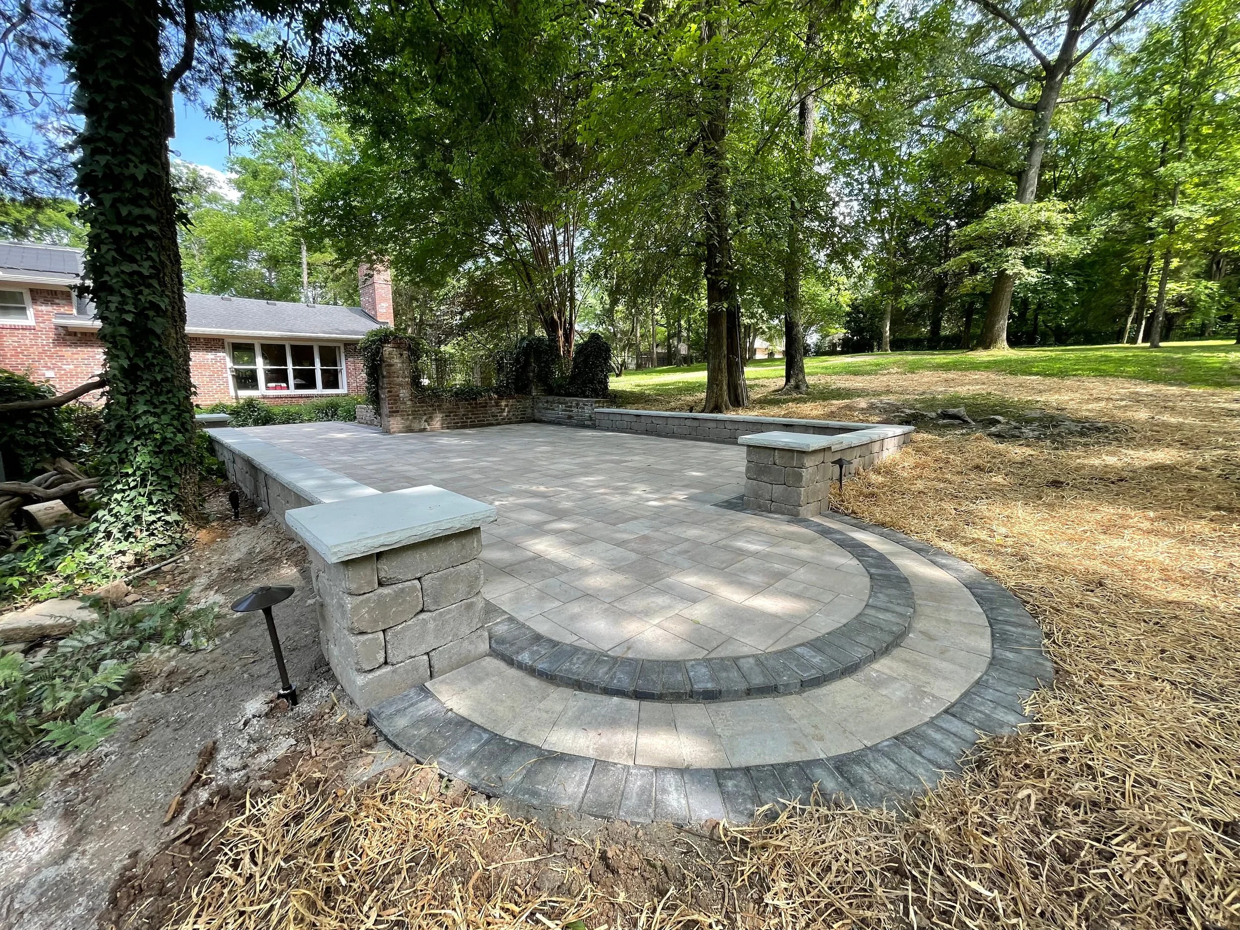 Custom paver courtyard featuring a circular stepped entry, natural stacked stone retaining walls, and tiered patio layout. A fully engineered outdoor living space built to impress from every angle. Premium hardscape design and installation by Mammoth