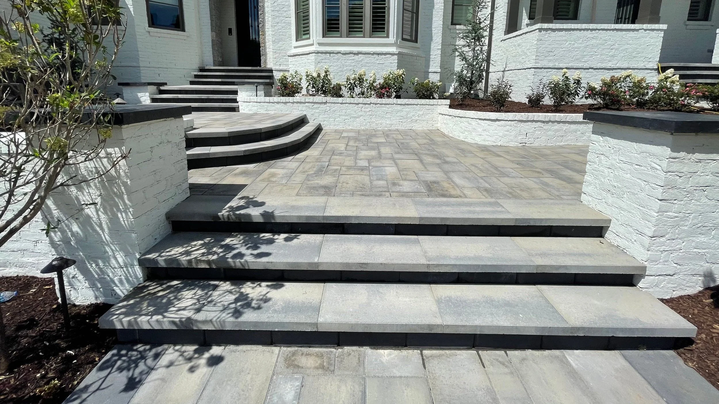 
Luxury residential entryway installation featuring cascading wide-format bluestone steps, curved stucco-finish retaining walls, and large-format paver landing. Natural stone stair and hardscape entry design built for high-end curb appeal. Premium en
