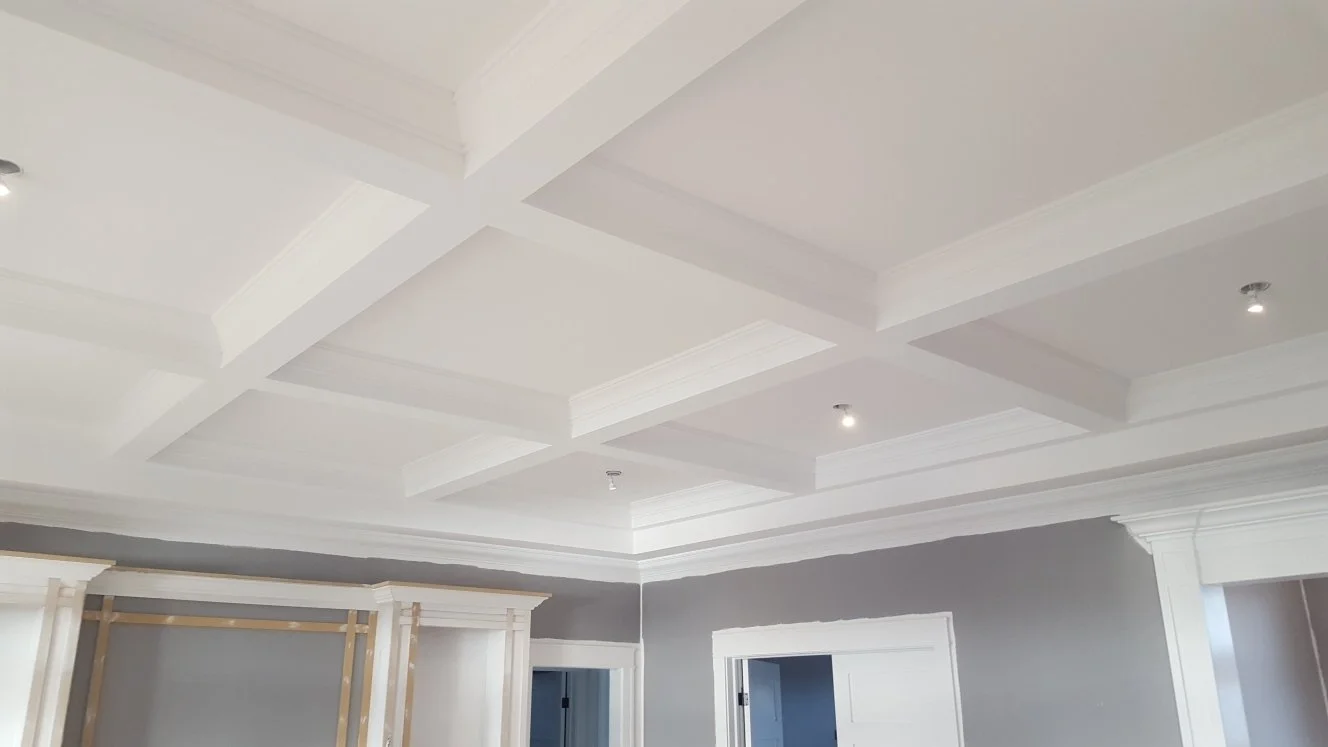 Interior of a room with a coffered ceiling, painted white, with recessed lighting and gray walls.