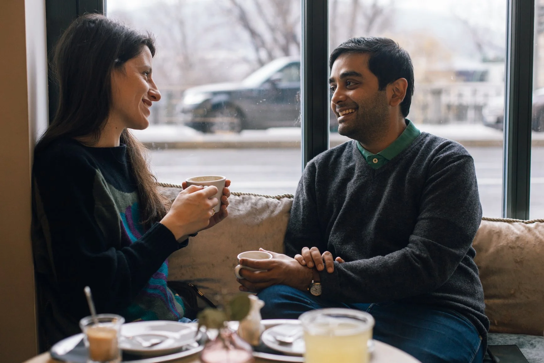 A man and woman sitting together in a coffee shop, smiling at each other, holding cups of coffee. EFT Couples Therapy in Royal Oak, Michigan and online statewide