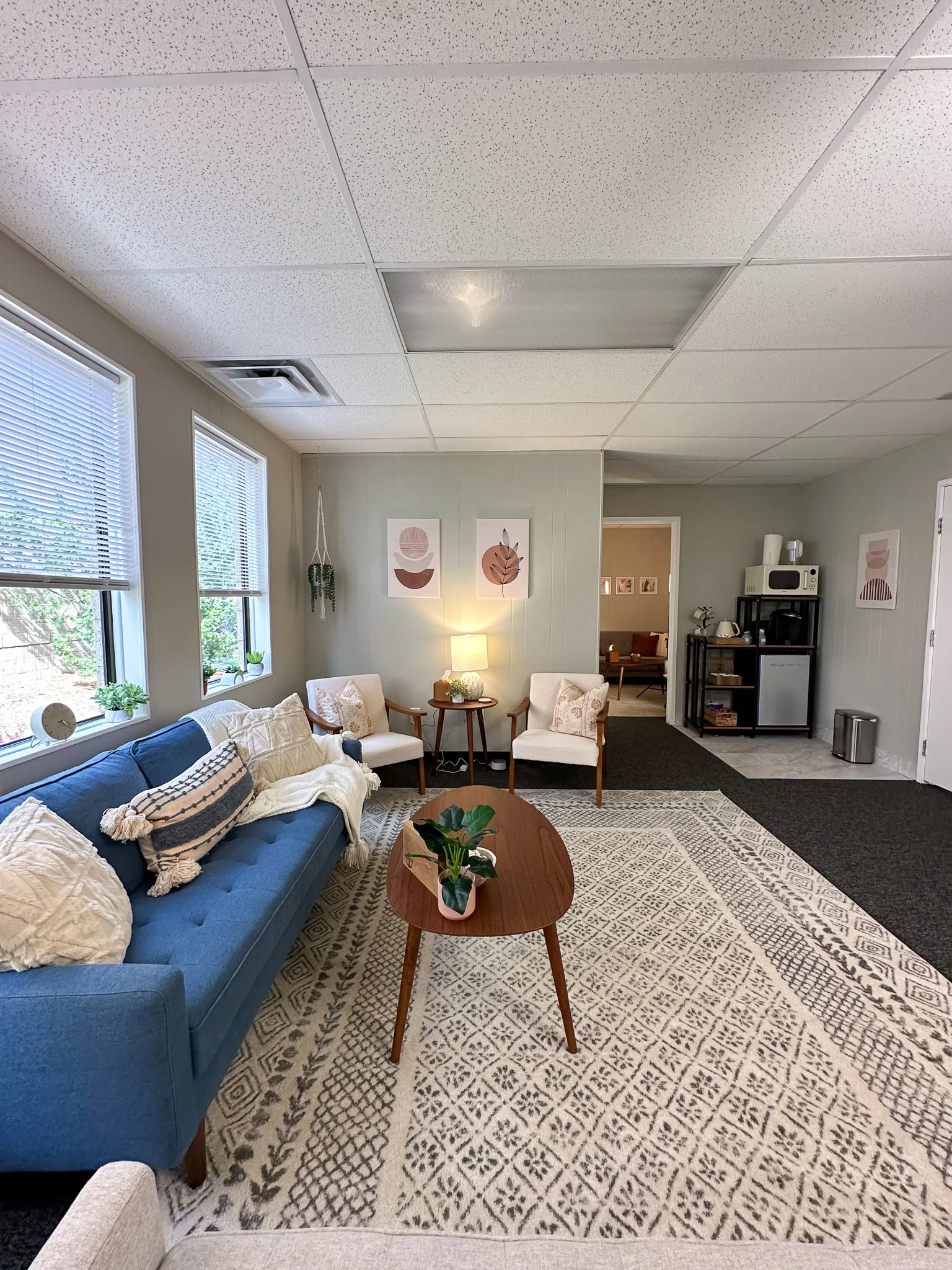 Living room with beige walls, beige area rug, and black tiled floor. There are two cream armchairs, a navy sofa with throw pillows, and a wooden coffee table with a houseplant.  EFT Couples Therapy in Royal Oak