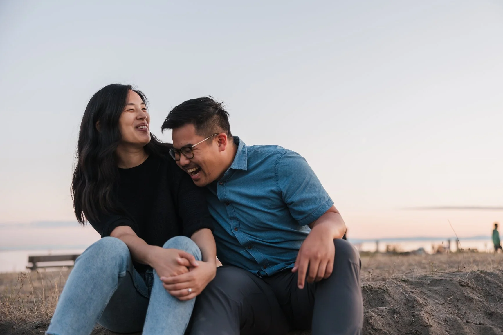 A man and woman sitting on the ground at the beach, laughing and enjoying each other's company during sunset. EFT Couples Therapy in Royal Oak, Michigan and online statewide