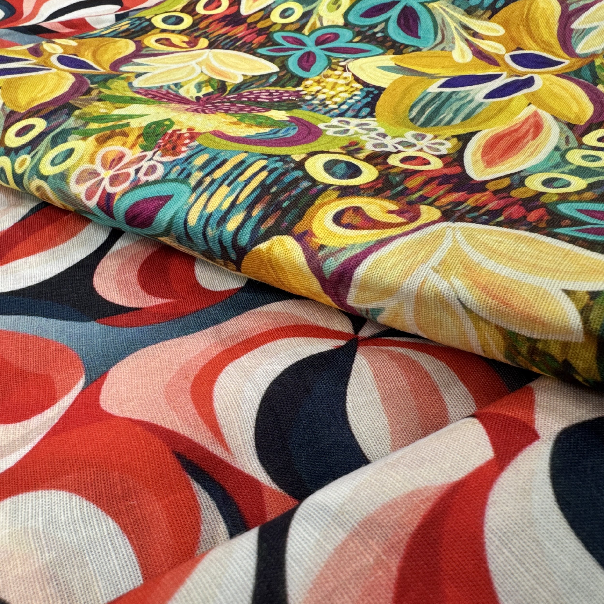 Close-up of colorful patterned fabric with floral and abstract designs, including yellow, red, black, and white colors, laid out on a surface.
