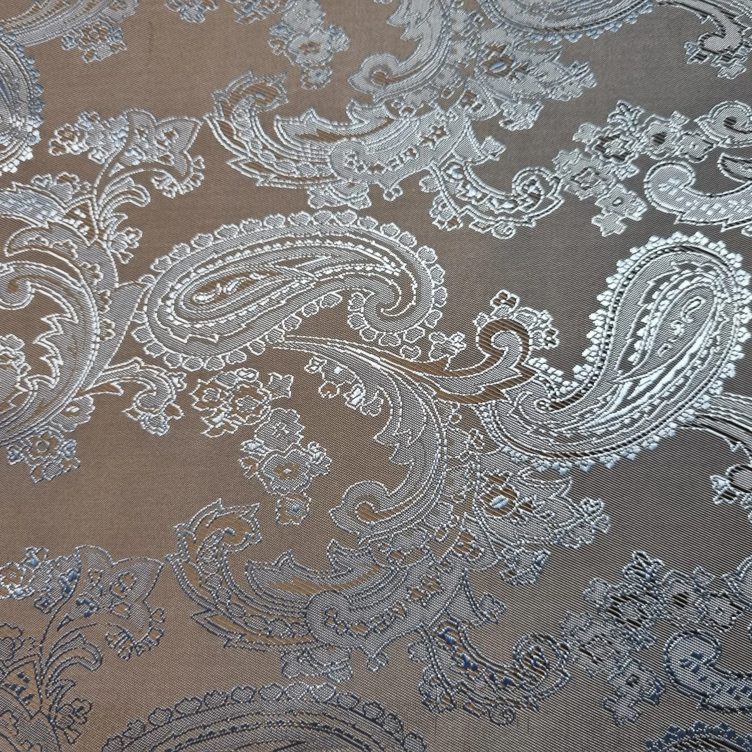 Close-up of intricate silver embroidery and paisley patterns on a beige fabric, resembling a lace or tapestry design.