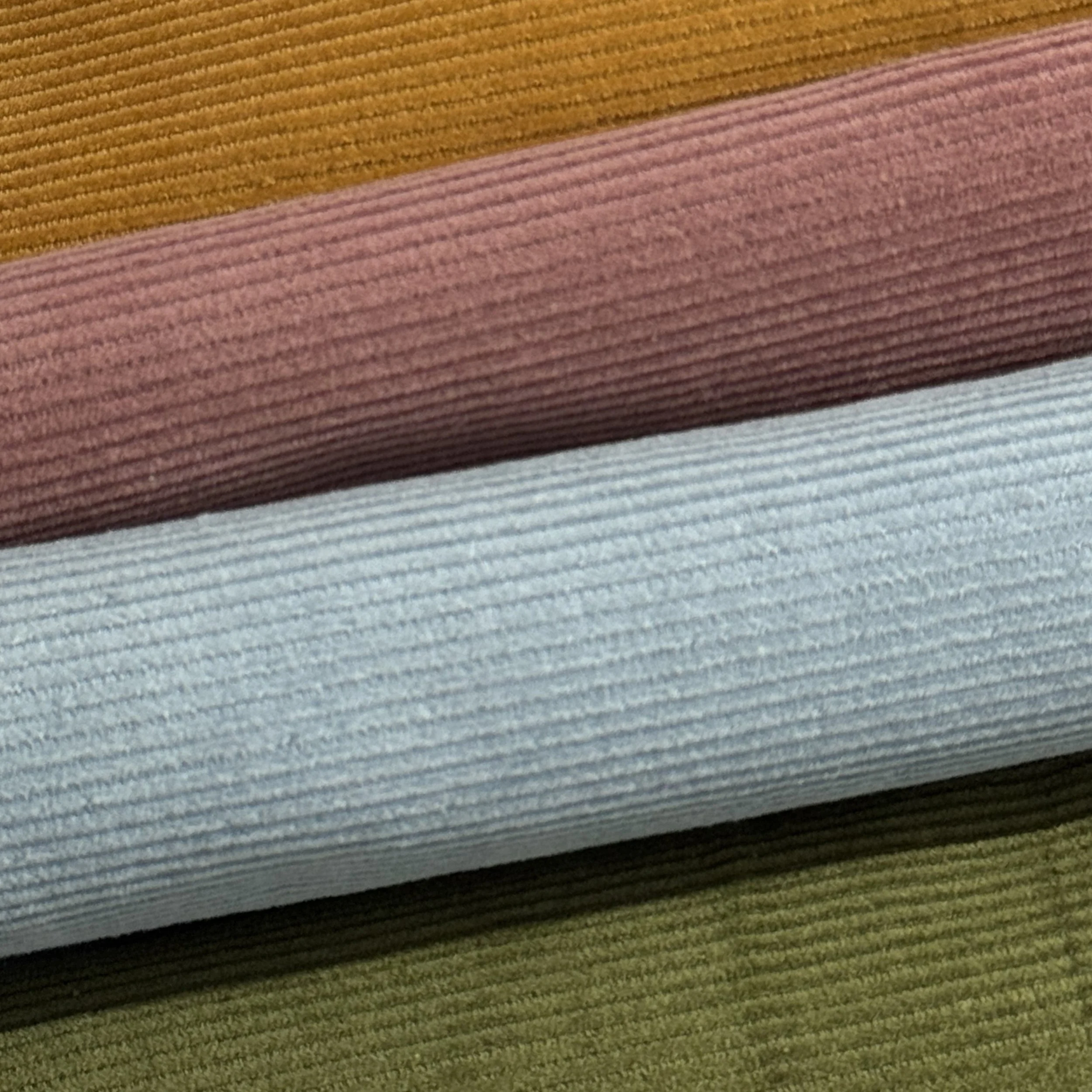 Close-up of folded fabric in multiple colors including mustard yellow, pink, brown, gray, and green with a ribbed texture.