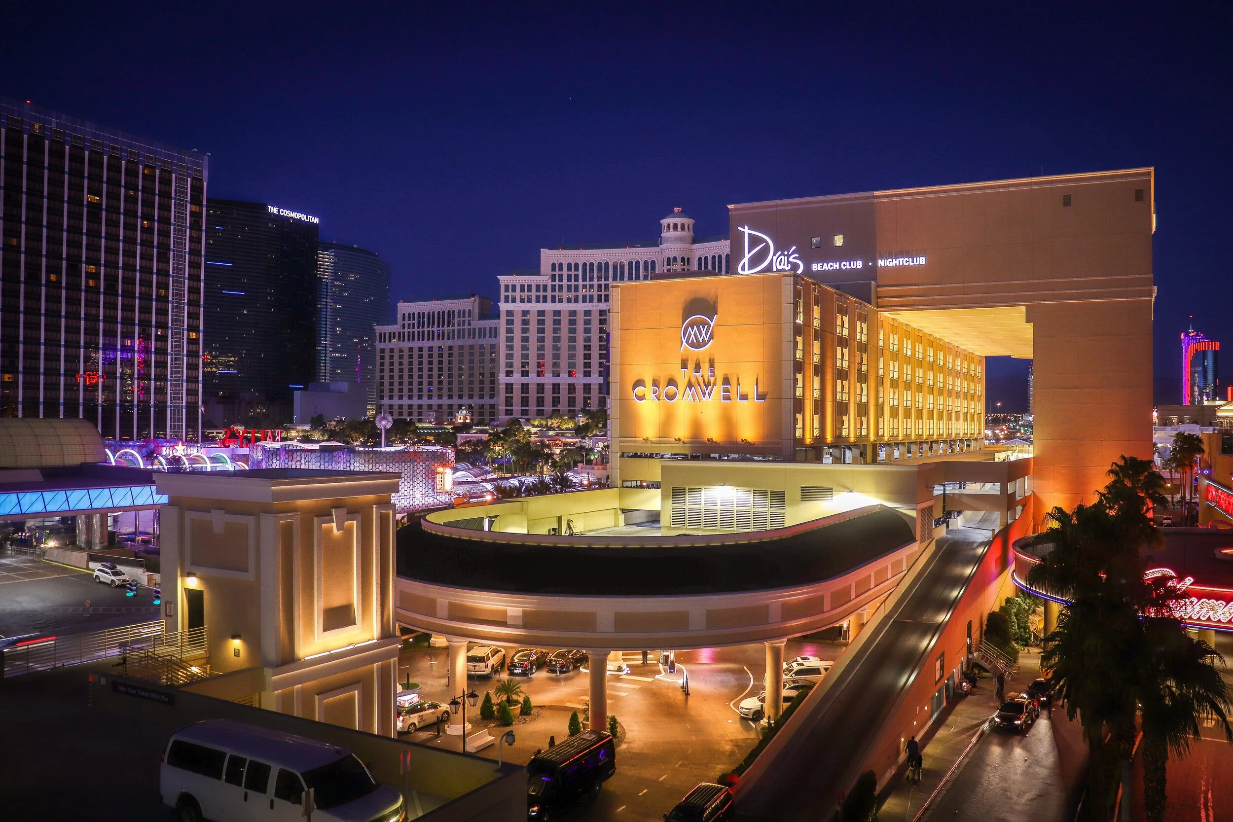 Night view of Las Vegas Strip with illuminated buildings, including Drai's Beach Club and The Cromwell, under a dark sky with some clouds and city lights.