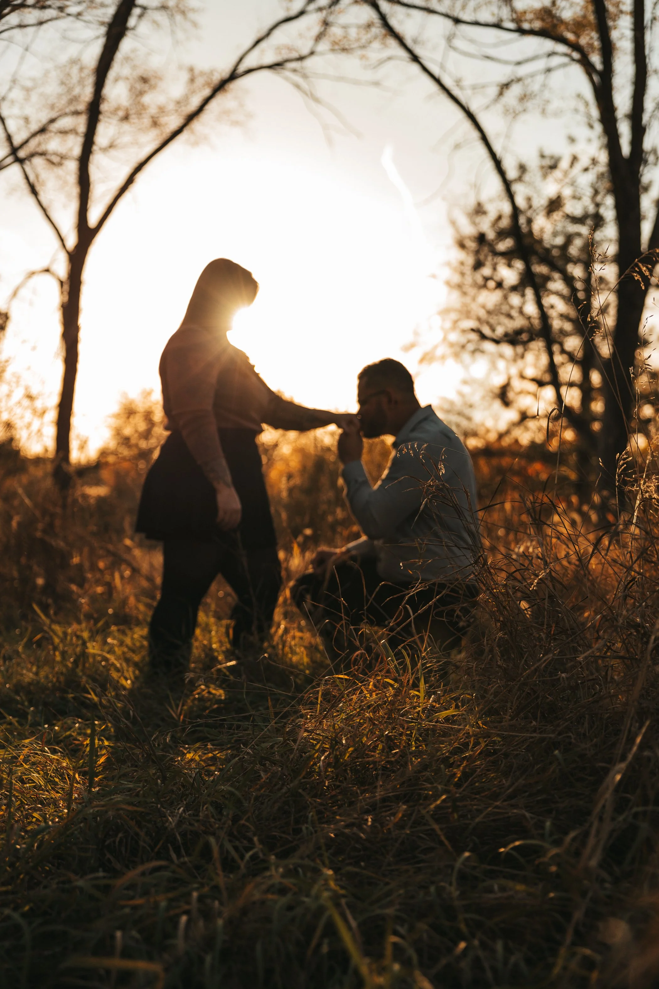 A man proposing to a woman during sunset in a wooded area.