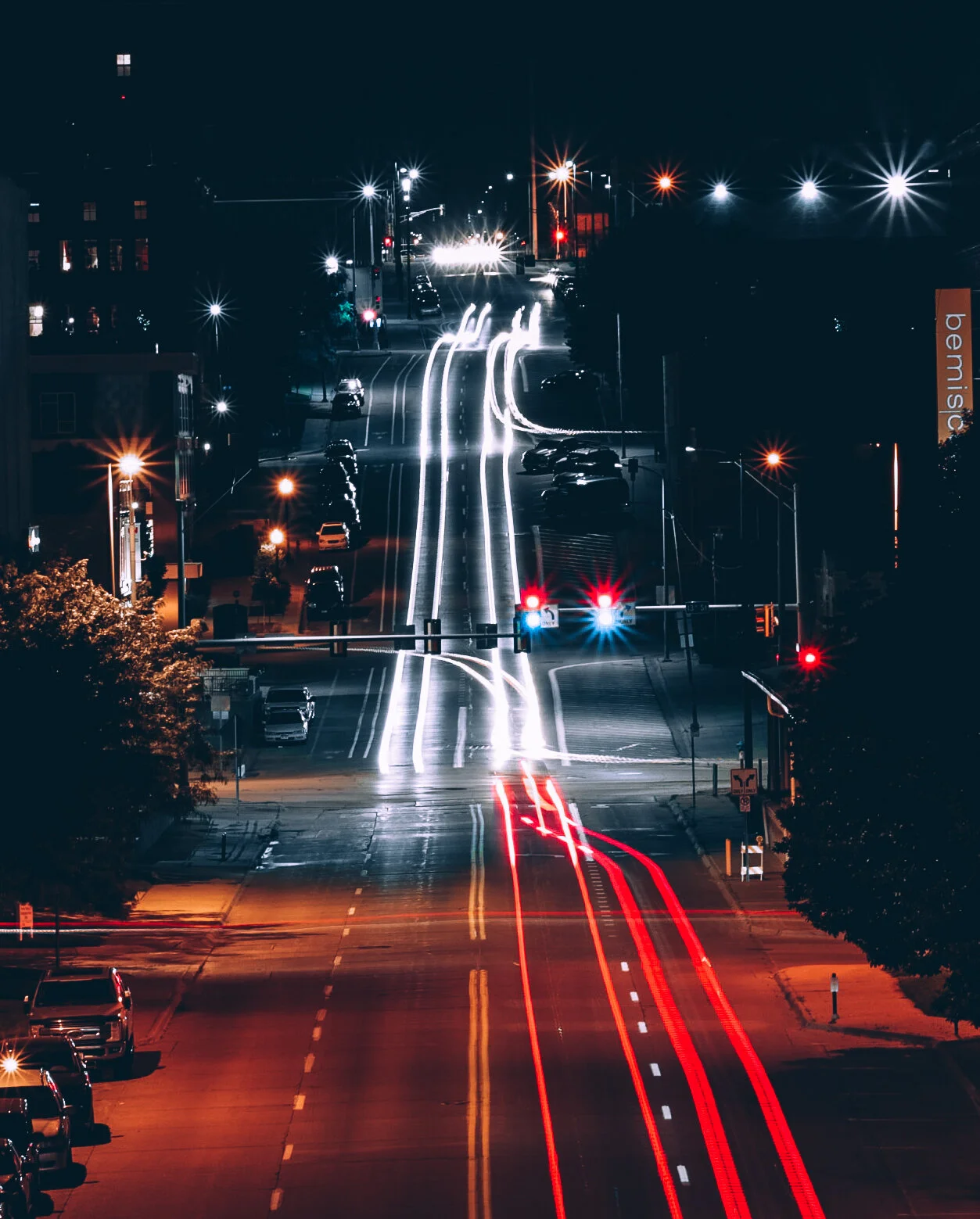Nighttime city street with light trails from moving vehicles, traffic signals, and illuminated buildings.