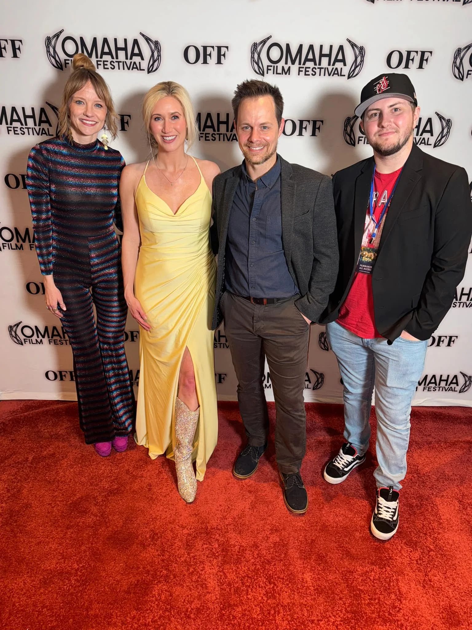 Four people standing on a red carpet at the Omaha Film Festival, posing for a group photo in front of a Step and Repeat backdrop with the festival's logo.