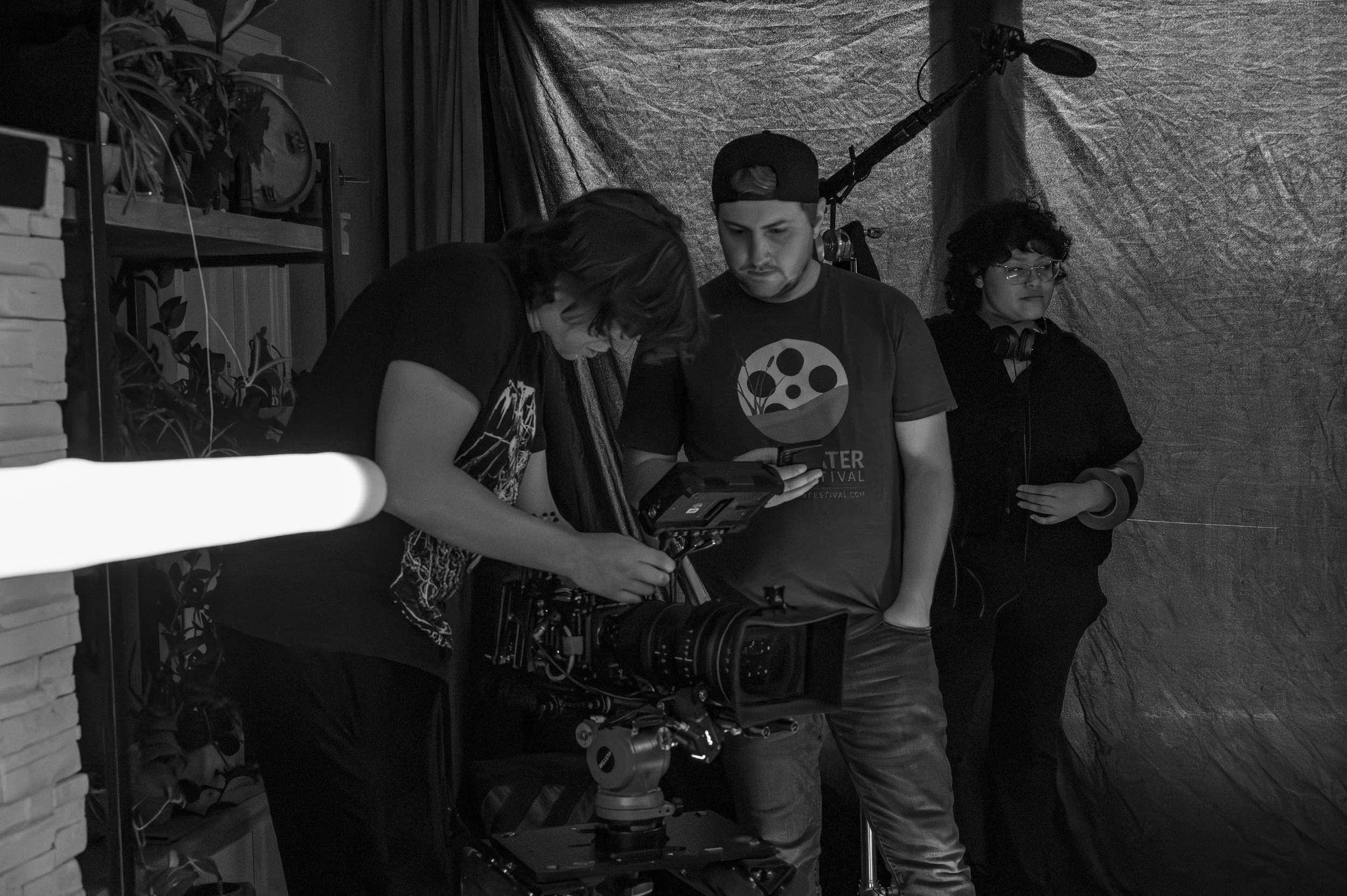 People working with film equipment in a studio, including a camera and a person holding a monitor, with two others observing.