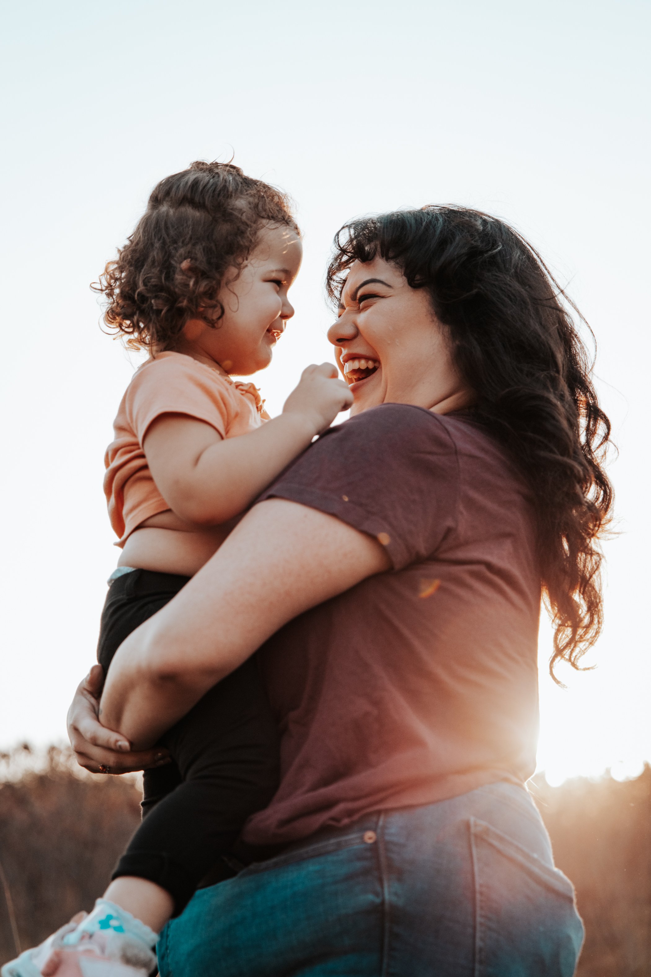 A woman and a young girl sharing a joyful moment outdoors during sunset.